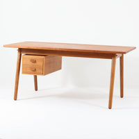 Poul M. Voltherがデザインし、FDB Moblerによって製作された片袖デスク。チーク材の天板と収納部、オーク材の脚部を組み合わせた構成に、真鍮の金具がさりげないアクセントを添える北欧ビンテージらしい一台です。幅160cmのゆとりあるサイズ感に対して、脚部や幕板は軽やかに設計されており、空間に圧迫感を与えません。片側に備えた引き出しユニットは、取り付けた状態でもスライドさせて位置調整が可能で、左右どちら側にも付け替えられる柔軟な構造となっています。さらに引き出しを取り外すことで、デスクとしてだけでなくダイニングテーブルとしても使用でき、暮らしの変化に合わせた使い方ができる点も魅力です。素材ごとの質感の違いと、経年により深みを増した木肌の表情が調和した、長く使い続けたくなるデザインです。