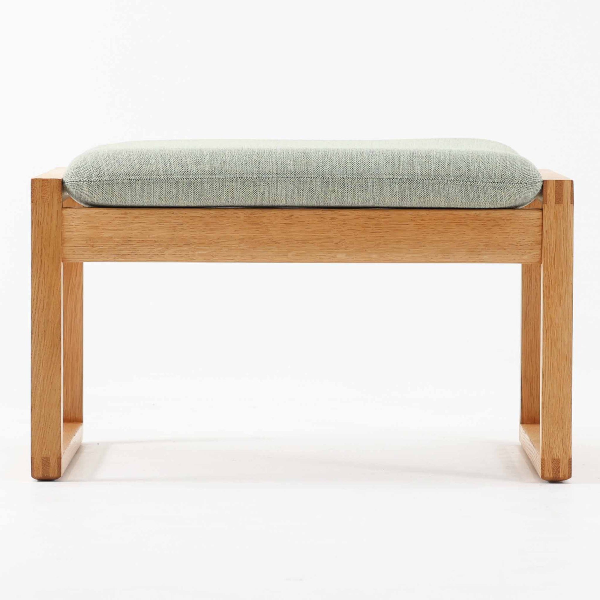 Borge Mogensenがデザインし、Fredericia社より製作されたModel 2248のオットマンです。オーク材を使用した堅牢なフレームは、北欧家具らしいシンプルで実用性を重視したデザインが魅力。直線的で無駄のない構造と、丁寧な木工による美しい仕上げが、モーエンセンの哲学を感じさせます。クッションにはやわらかなファブリックを張り、快適な座り心地を実現。オットマンとして足を休める用途はもちろん、スツールや補助椅子としても活躍します。同シリーズのラウンジチェアと組み合わせることで、より快適なくつろぎの空間を演出できる、北欧ビンテージならではの機能美を備えた一品です。
