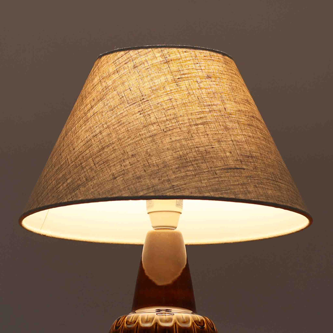 Einar JohansenがSoholm Keramik（スーホルム・セラミック）のために手掛けたモデル1015は、深いブラウンの釉薬に美しい光沢が宿り、ベースを覆う羽根模様のようなレリーフが立体的な表情を生み出す北欧ビンテージの名品で、すっきりと立ち上がるシルエットと陶磁器ならではの重厚感が空間に落ち着いた存在感をもたらします。リネンシェードを通したやわらかな灯りはベッドサイドやリビングに 温かみを添え、経年の風合いが一点物としての魅力をより一層引き立てています。