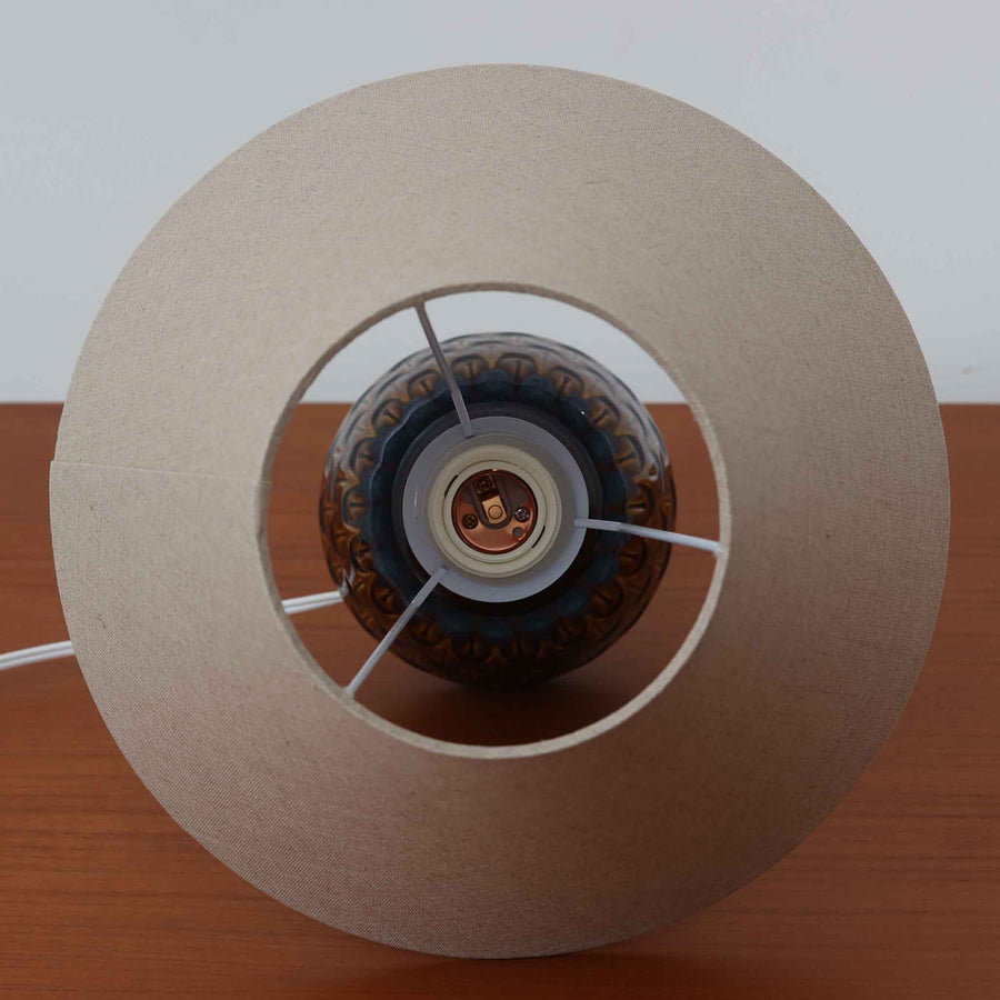 Einar JohansenがSoholm Keramik（スーホルム・セラミック）のために手掛けたモデル1015は、深いブラウンの釉薬に美しい光沢が宿り、ベースを覆う羽根模様のようなレリーフが立体的な表情を生み出す北欧ビンテージの名品で、すっきりと立ち上がるシルエットと陶磁器ならではの重厚感が空間に落ち着いた存在感をもたらします。リネンシェードを通したやわらかな灯りはベッドサイドやリビングに 温かみを添え、経年の風合いが一点物としての魅力をより一層引き立てています。