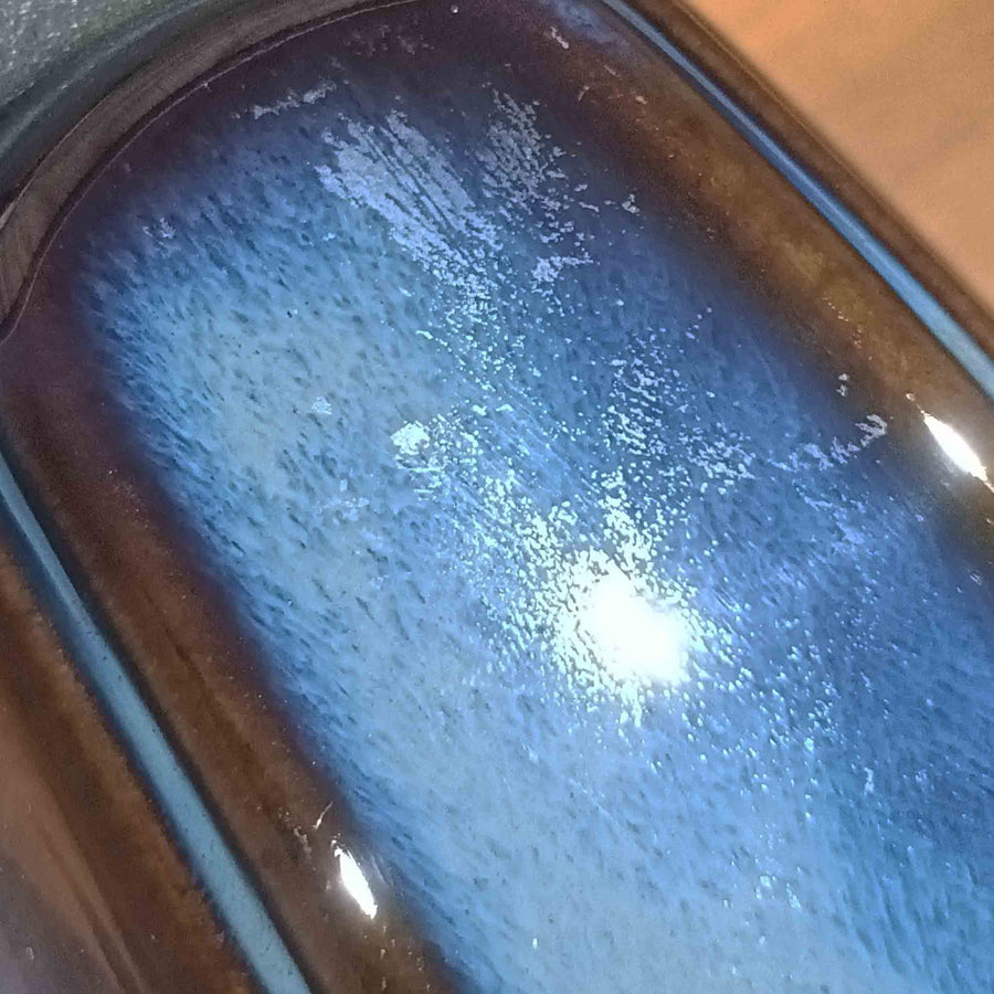 Einar JohansenがSoholm Keramik（スーホルム・セラミック）のためにデザインしたモデル1031は、深みのあるブルーの釉薬と立体的な面取りが織りなす陰影が美しい陶磁器ベースが特徴で、上部のマットな質感との対比がモダンで彫刻的な存在感を放つ北欧ビンテージ品です。プリーツシェードを透ける柔らかな灯りが落ち着いた雰囲気をつくり、ベッドサイドやリビングのアクセント照明として取り入れやすく、経年で深まった釉薬の表情が一点物ならではの魅力を一層引き立てています。