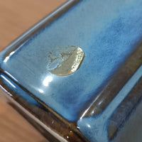 Einar JohansenがSoholm Keramik（スーホルム・セラミック）のためにデザインしたモデル1031は、深みのあるブルーの釉薬と立体的な面取りが織りなす陰影が美しい陶磁器ベースが特徴で、上部のマットな質感との対比がモダンで彫刻的な存在感を放つ北欧ビンテージ品です。プリーツシェードを透ける柔らかな灯りが落ち着いた雰囲気をつくり、ベッドサイドやリビングのアクセント照明として取り入れやすく、経年で深まった釉薬の表情が一点物ならではの魅力を一層引き立てています。