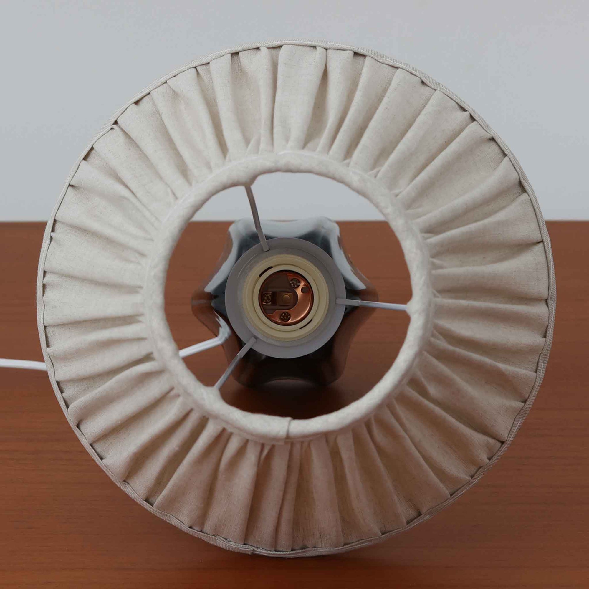 Einar JohansenがSoholm Keramik（スーホルム・セラミック）のためにデザインしたモデル1031は、深みのあるブルーの釉薬と立体的な面取りが織りなす陰影が美しい陶磁器ベースが特徴で、上部のマットな質感との対比がモダンで彫刻的な存在感を放つ北欧ビンテージ品です。プリーツシェードを透ける柔らかな灯りが落ち着いた雰囲気をつくり、ベッドサイドやリビングのアクセント照明として取り入れやすく、経年で深まった釉薬の表情が一点物ならではの魅力を一層引き立てています。