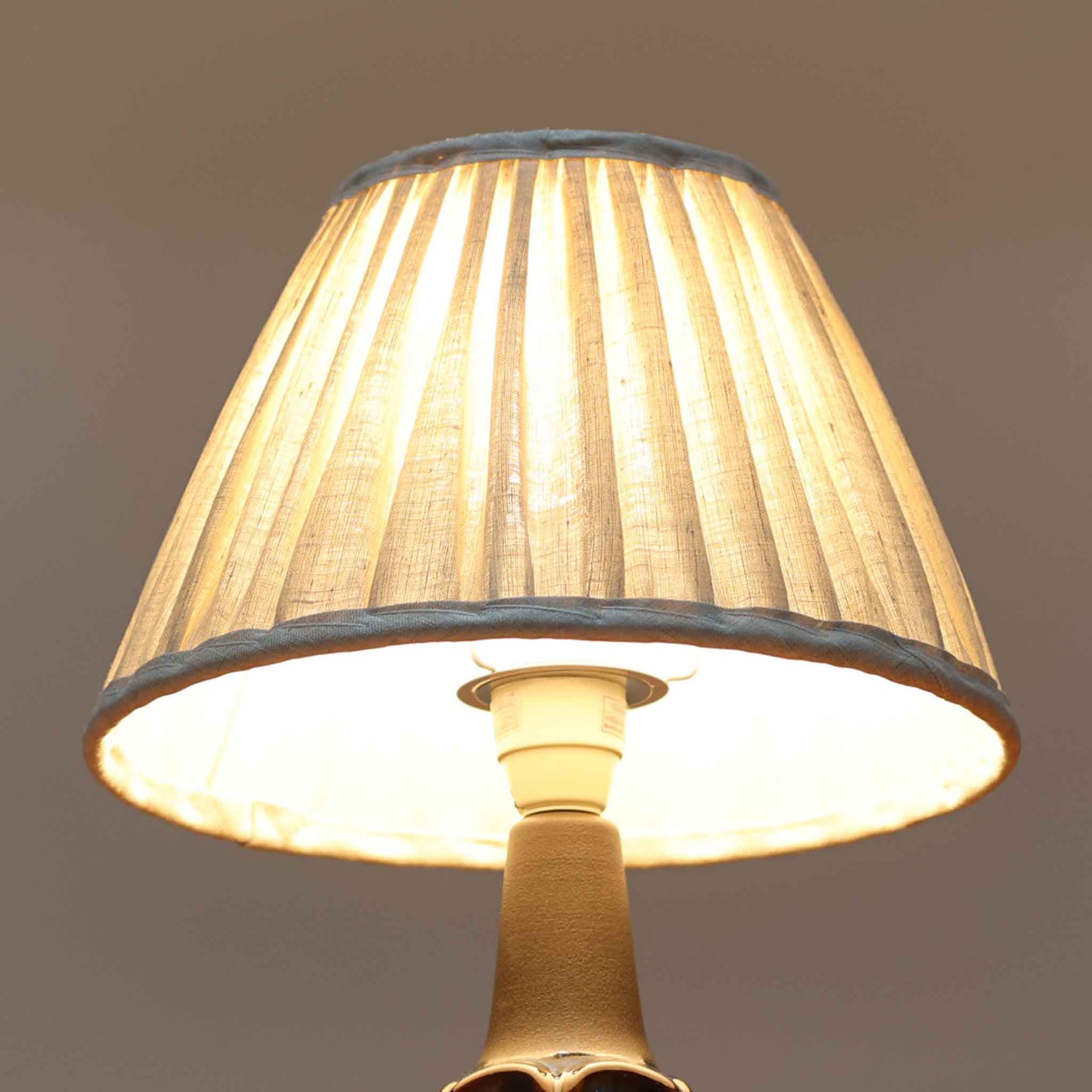 Einar JohansenがSoholm Keramik（スーホルム・セラミック）のためにデザインしたモデル1031は、深みのあるブルーの釉薬と立体的な面取りが織りなす陰影が美しい陶磁器ベースが特徴で、上部のマットな質感との対比がモダンで彫刻的な存在感を放つ北欧ビンテージ品です。プリーツシェードを透ける柔らかな灯りが落ち着いた雰囲気をつくり、ベッドサイドやリビングのアクセント照明として取り入れやすく、経年で深まった釉薬の表情が一点物ならではの魅力を一層引き立てています。