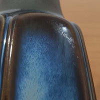 Einar JohansenがSoholm Keramik（スーホルム・セラミック）のためにデザインしたモデル1031は、深みのあるブルーの釉薬と立体的な面取りが織りなす陰影が美しい陶磁器ベースが特徴で、上部のマットな質感との対比がモダンで彫刻的な存在感を放つ北欧ビンテージ品です。プリーツシェードを透ける柔らかな灯りが落ち着いた雰囲気をつくり、ベッドサイドやリビングのアクセント照明として取り入れやすく、経年で深まった釉薬の表情が一点物ならではの魅力を一層引き立てています。