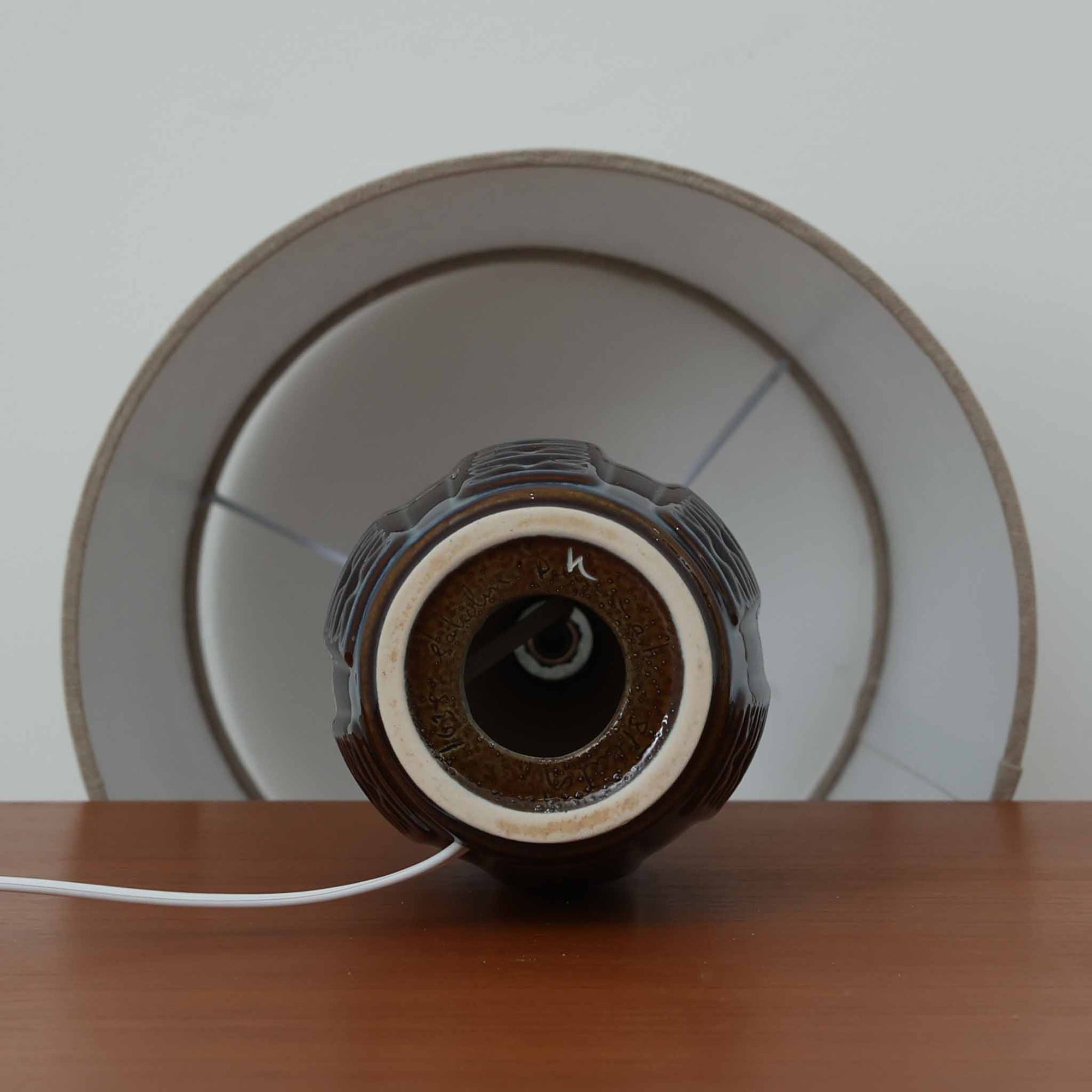 Einar JohansenがSoholm Keramik（スーホルム・セラミック）のために手掛けたモデル1038は、深みのあるブルーの釉薬が重なり合うように陰影をつくる陶磁器ベースと、上部のマットな質感とのコントラストが美しい北欧ビンテージ品で、四面に施された力強いレリーフ装飾が彫刻的な存在感を与えます。リネンシェード越しに広がる柔らかな灯りが空間を優しく包み込み、リビングやベッドサイドのアクセント照明として取り入れやすく、経年で深まった釉薬の表情が一点物ならではの味わいを一層引き立てています。