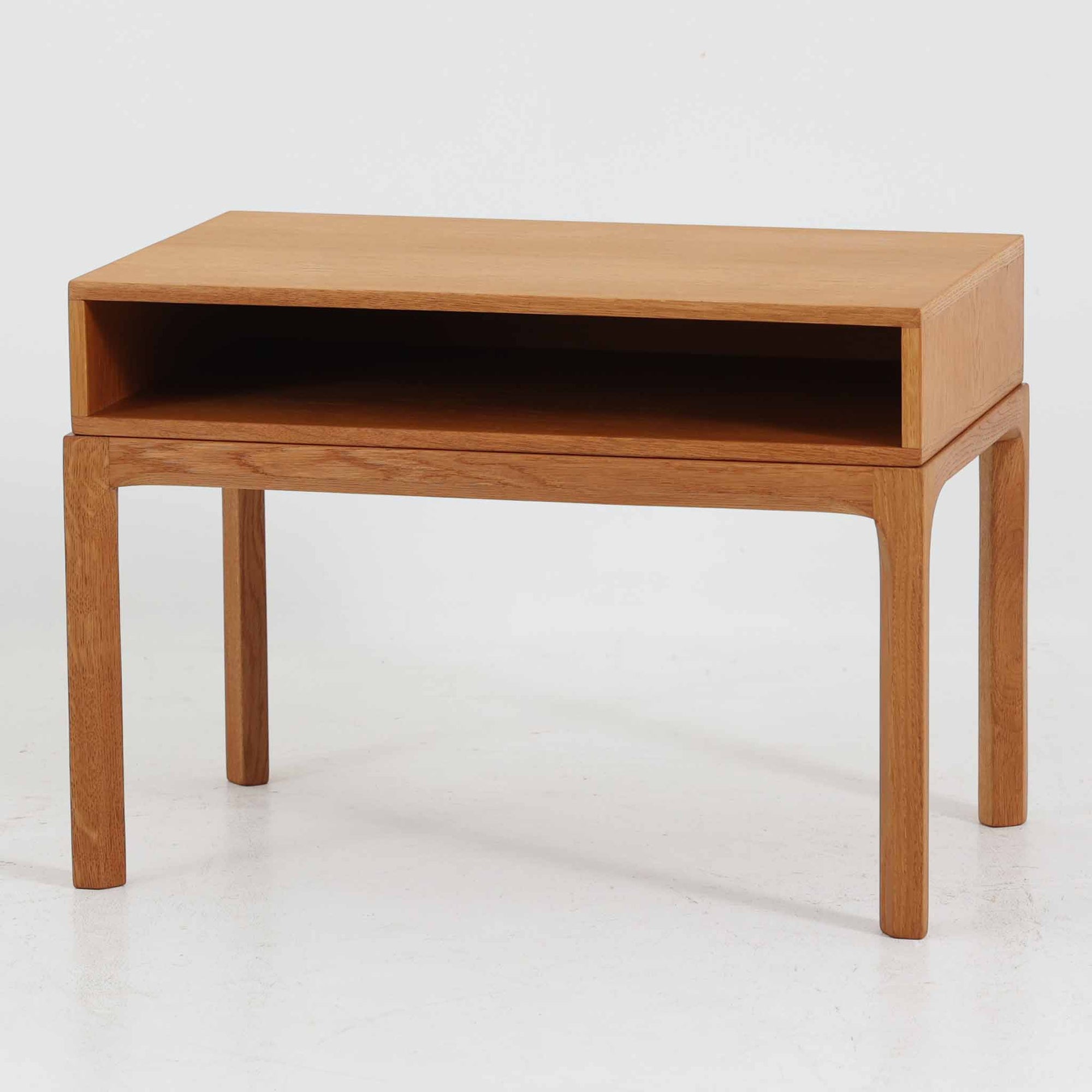 デンマークのデザイナー、カイ・クリスチャンセンによるデザイン、Aksel Kjersgaard社製のサイドテーブル「No.383」です。オーク材を用いた端正な造りで、脚部の滑らかなカーブや接合部の美しいラインなど、北欧家具の職人技が随所に感じられます。天板下には小物を収納できるスペースが設けられ、実用性とデザイン性を兼ね備えた構造です。経年によるオークの柔らかな風合いが魅力で、ベッドサイドやリビングのアクセントとしてもおすすめの一台です。