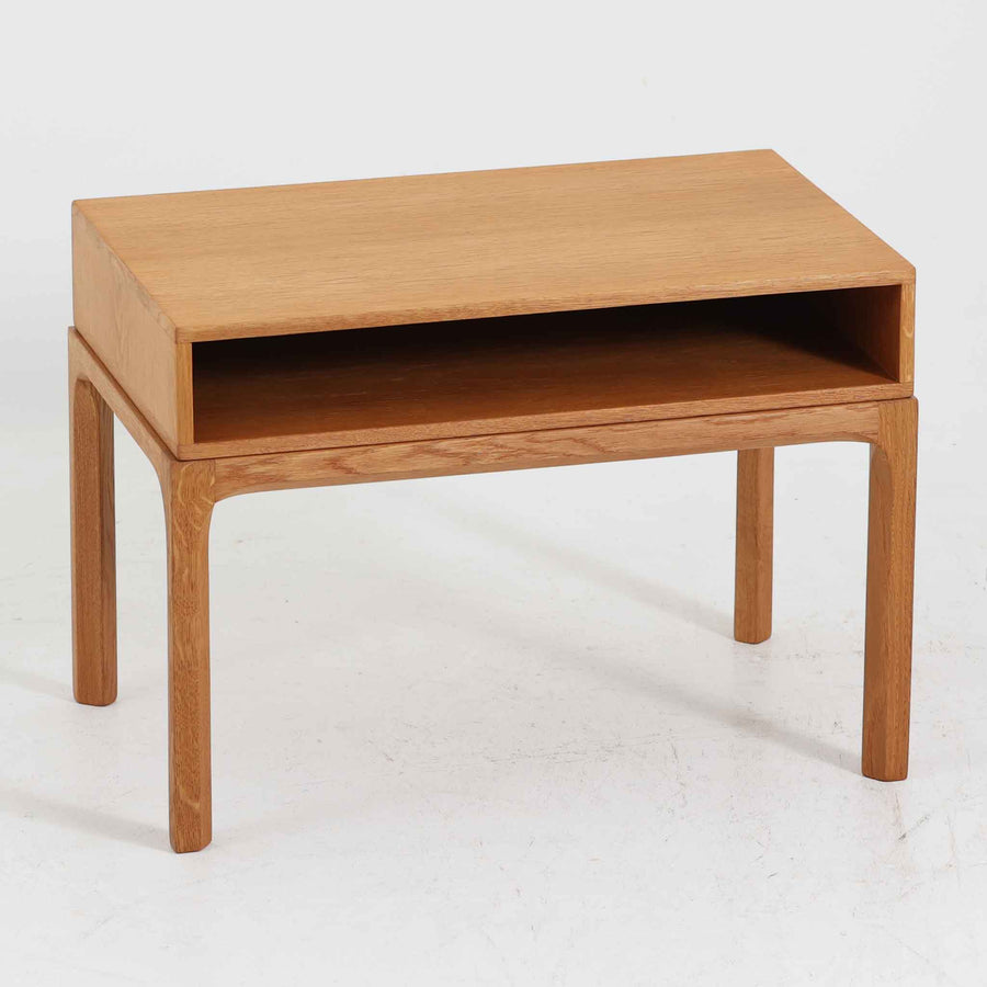 デンマークのデザイナー、カイ・クリスチャンセンによるデザイン、Aksel Kjersgaard社製のサイドテーブル「No.383」です。オーク材を用いた端正な造りで、脚部の滑らかなカーブや接合部の美しいラインなど、北欧家具の職人技が随所に感じられます。天板下には小物を収納できるスペースが設けられ、実用性とデザイン性を兼ね備えた構造です。経年によるオークの柔らかな風合いが魅力で、ベッドサイドやリビングのアクセントとしてもおすすめの一台です。