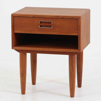 デンマーク製のサイドチェストで、シンプルなボックス構成にチーク材の豊かな風合いが映える北欧ビンテージらしい一台です。オープンスペースは本や小物の収納に便利で、引き出しには金属フレームを組み合わせたユニークな取手がアクセントとして効いています。丸みを帯びた角や細く伸びたテーパードレッグが軽快な印象を与え、ベッドサイドやソファ横でのサイドテーブル使いにも最適。経年変化の味わい深い木肌が空間に温かさと上質さを添えます。