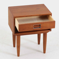 デンマーク製のサイドチェストで、シンプルなボックス構成にチーク材の豊かな風合いが映える北欧ビンテージらしい一台です。オープンスペースは本や小物の収納に便利で、引き出しには金属フレームを組み合わせたユニークな取手がアクセントとして効いています。丸みを帯びた角や細く伸びたテーパードレッグが軽快な印象を与え、ベッドサイドやソファ横でのサイドテーブル使いにも最適。経年変化の味わい深い木肌が空間に温かさと上質さを添えます。