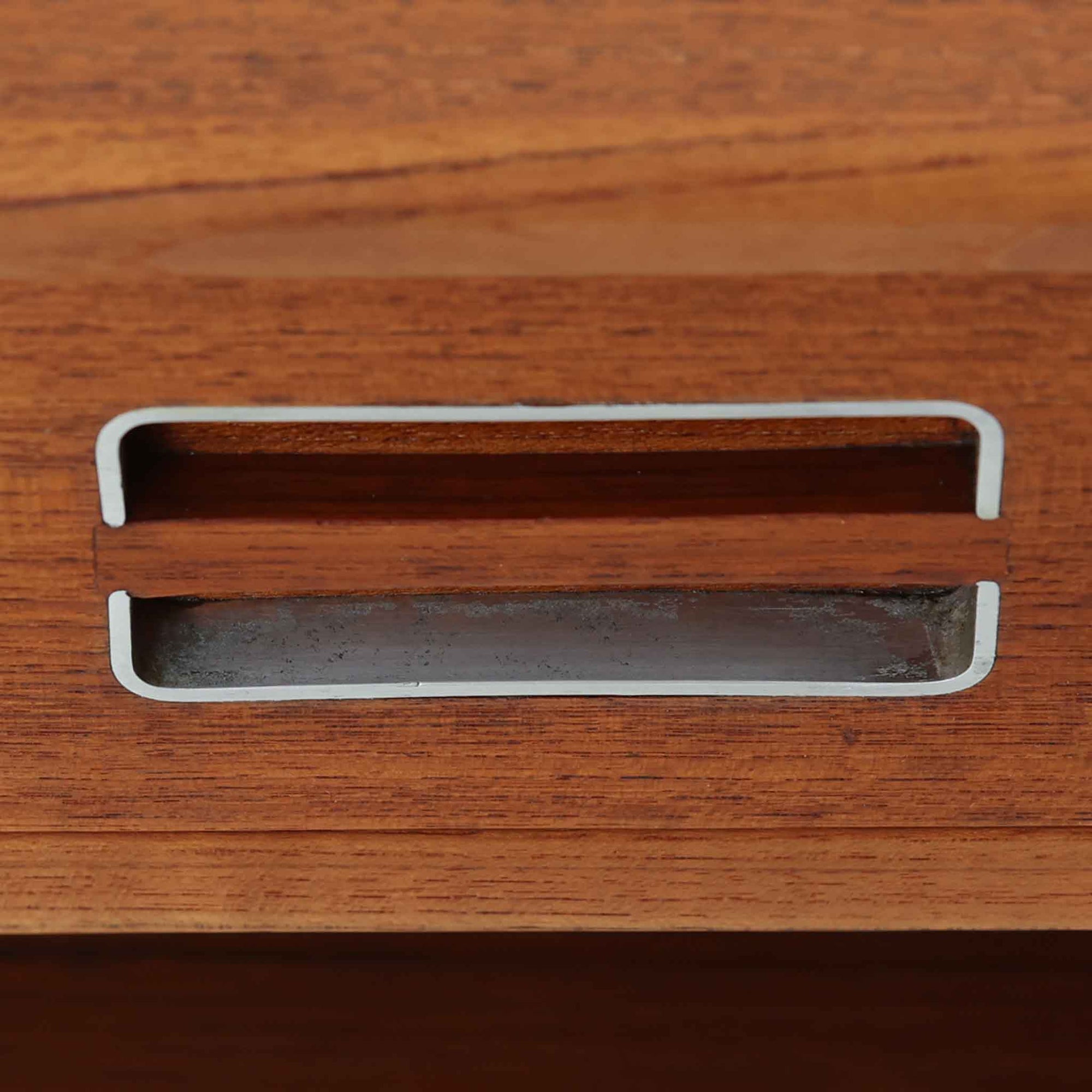 デンマーク製のサイドチェストで、シンプルなボックス構成にチーク材の豊かな風合いが映える北欧ビンテージらしい一台です。オープンスペースは本や小物の収納に便利で、引き出しには金属フレームを組み合わせたユニークな取手がアクセントとして効いています。丸みを帯びた角や細く伸びたテーパードレッグが軽快な印象を与え、ベッドサイドやソファ横でのサイドテーブル使いにも最適。経年変化の味わい深い木肌が空間に温かさと上質さを添えます。