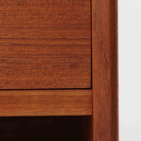 デンマーク製のサイドチェストで、シンプルなボックス構成にチーク材の豊かな風合いが映える北欧ビンテージらしい一台です。オープンスペースは本や小物の収納に便利で、引き出しには金属フレームを組み合わせたユニークな取手がアクセントとして効いています。丸みを帯びた角や細く伸びたテーパードレッグが軽快な印象を与え、ベッドサイドやソファ横でのサイドテーブル使いにも最適。経年変化の味わい深い木肌が空間に温かさと上質さを添えます。