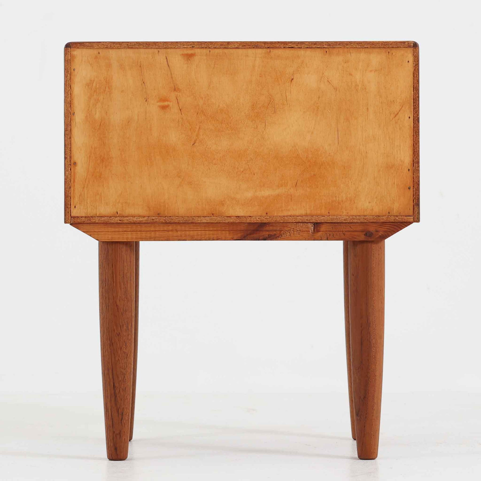 デンマーク製のサイドチェストで、シンプルなボックス構成にチーク材の豊かな風合いが映える北欧ビンテージらしい一台です。オープンスペースは本や小物の収納に便利で、引き出しには金属フレームを組み合わせたユニークな取手がアクセントとして効いています。丸みを帯びた角や細く伸びたテーパードレッグが軽快な印象を与え、ベッドサイドやソファ横でのサイドテーブル使いにも最適。経年変化の味わい深い木肌が空間に温かさと上質さを添えます。