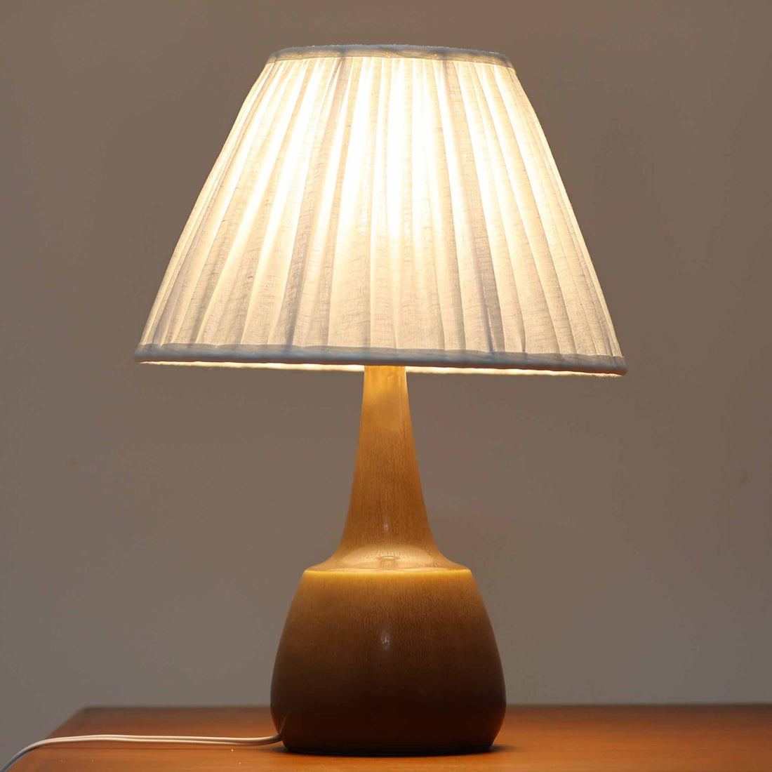 Per Lindemann SchmidtがPalshusのために手掛けたモデル「PL-5 SL 2」は、均整の取れたシルエットと滑らかに焼き締められたマットブラウンの陶肌が静かな存在感を放つテーブルランプで、首元にほんのり入る明るい釉薬のグラデーションが柔らかな表情を添える北欧ビンテージ品です。プリーツシェード越しに広がる落ち着いた灯りはリビングやベッドサイドに心地よい温もりをもたらし、シンプルながら洗練された造形美と経年で深まった風合いを長く楽しめる一台です。