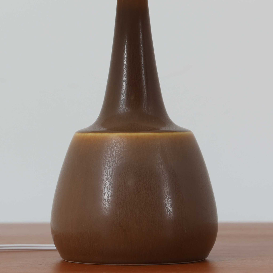 Per Lindemann SchmidtがPalshusのために手掛けたモデル「PL-5 SL 2」は、均整の取れたシルエットと滑らかに焼き締められたマットブラウンの陶肌が静かな存在感を放つテーブルランプで、首元にほんのり入る明るい釉薬のグラデーションが柔らかな表情を添える北欧ビンテージ品です。プリーツシェード越しに広がる落ち着いた灯りはリビングやベッドサイドに心地よい温もりをもたらし、シンプルながら洗練された造形美と経年で深まった風合いを長く楽しめる一台です。