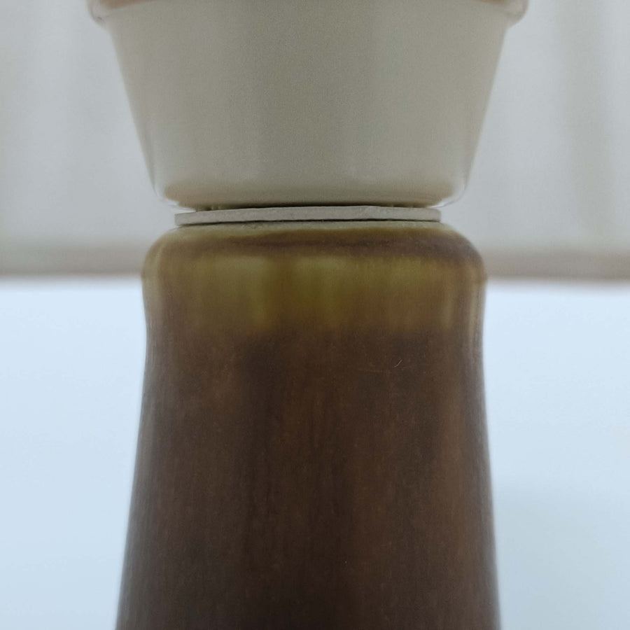 Per Lindemann SchmidtがPalshusのために手掛けたモデル「PL-5 SL 2」は、均整の取れたシルエットと滑らかに焼き締められたマットブラウンの陶肌が静かな存在感を放つテーブルランプで、首元にほんのり入る明るい釉薬のグラデーションが柔らかな表情を添える北欧ビンテージ品です。プリーツシェード越しに広がる落ち着いた灯りはリビングやベッドサイドに心地よい温もりをもたらし、シンプルながら洗練された造形美と経年で深まった風合いを長く楽しめる一台です。