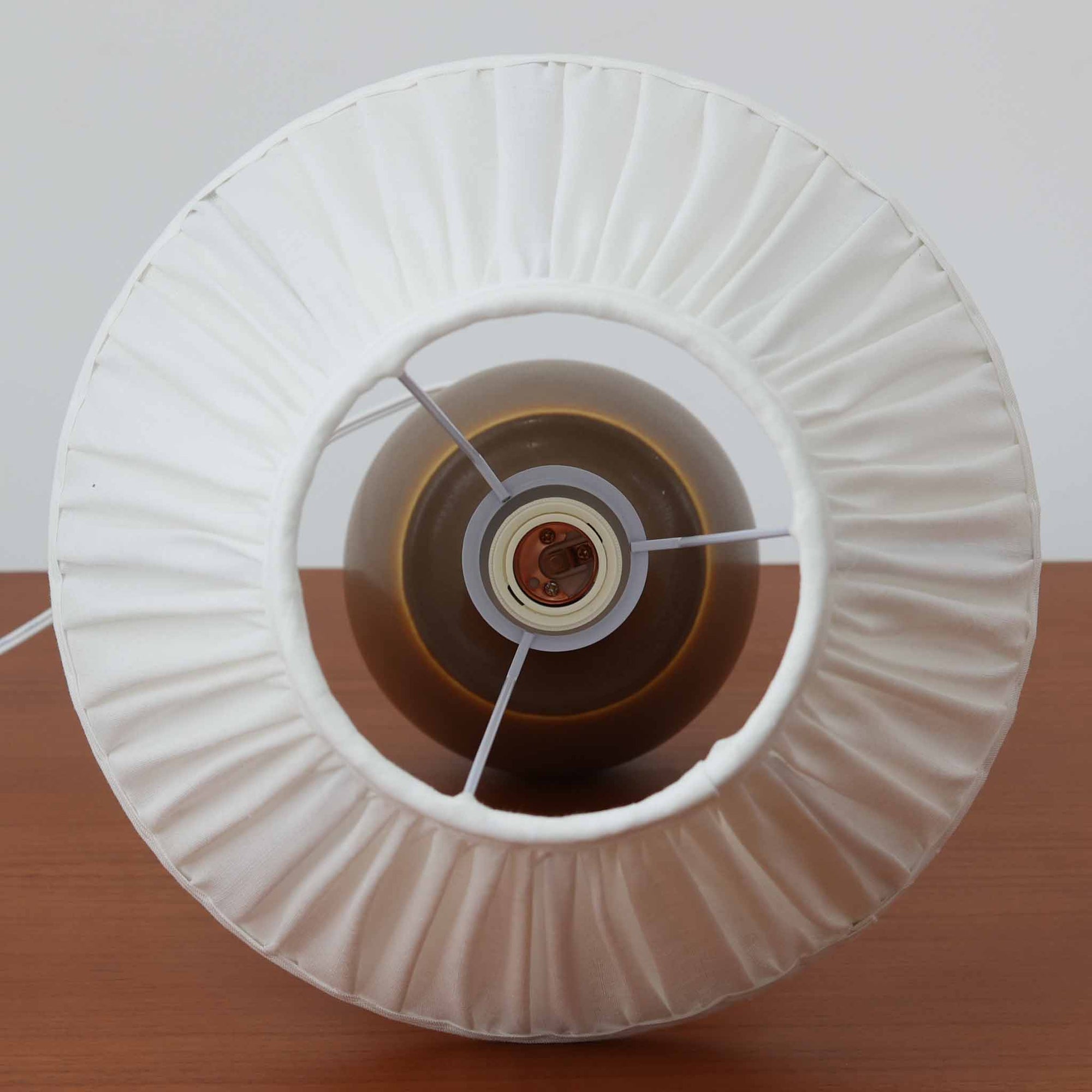 Per Lindemann SchmidtがPalshusのために手掛けたモデル「PL-5 SL 2」は、均整の取れたシルエットと滑らかに焼き締められたマットブラウンの陶肌が静かな存在感を放つテーブルランプで、首元にほんのり入る明るい釉薬のグラデーションが柔らかな表情を添える北欧ビンテージ品です。プリーツシェード越しに広がる落ち着いた灯りはリビングやベッドサイドに心地よい温もりをもたらし、シンプルながら洗練された造形美と経年で深まった風合いを長く楽しめる一台です。