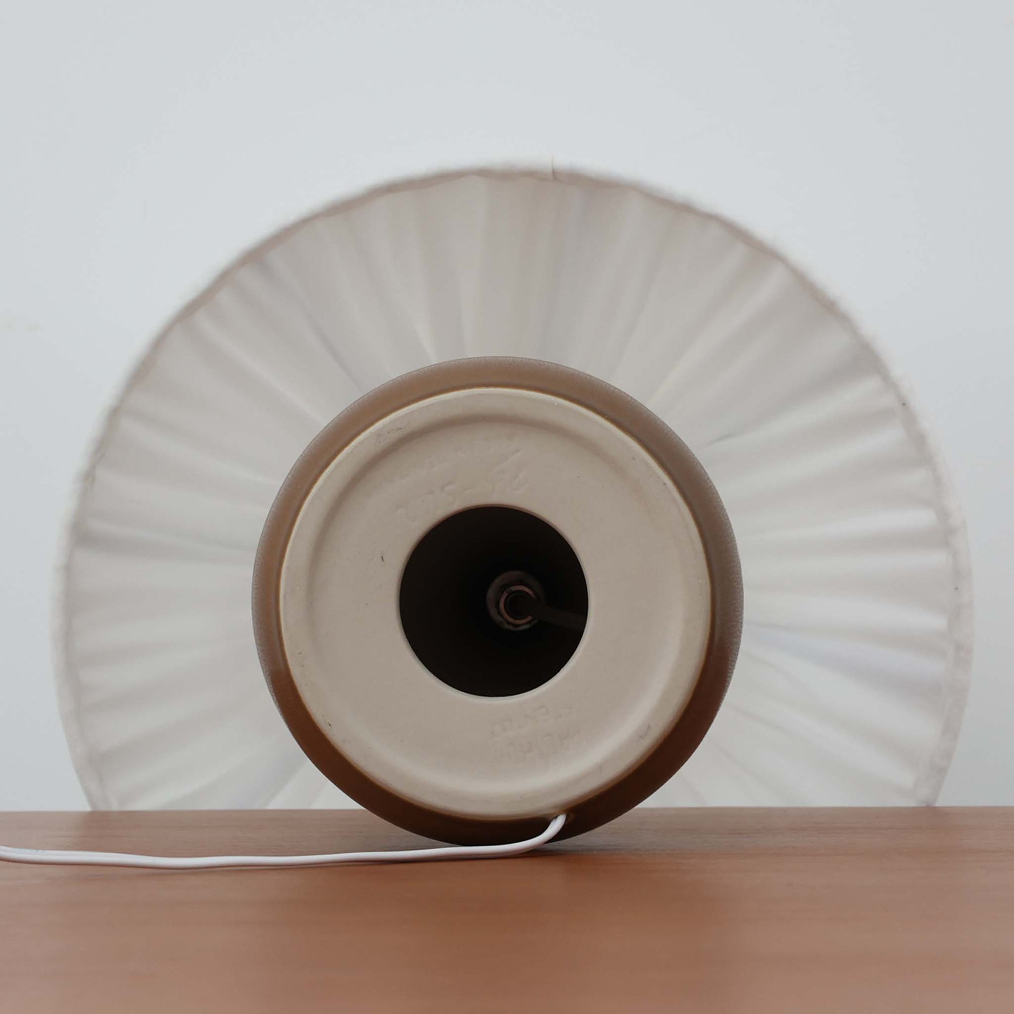 Per Lindemann SchmidtがPalshusのために手掛けたモデル「PL-5 SL 2」は、均整の取れたシルエットと滑らかに焼き締められたマットブラウンの陶肌が静かな存在感を放つテーブルランプで、首元にほんのり入る明るい釉薬のグラデーションが柔らかな表情を添える北欧ビンテージ品です。プリーツシェード越しに広がる落ち着いた灯りはリビングやベッドサイドに心地よい温もりをもたらし、シンプルながら洗練された造形美と経年で深まった風合いを長く楽しめる一台です。