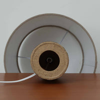 Jette HelleroeがAxellaのために手掛けたこちらのテーブルランプは、砂質の陶肌を生かした素朴で温かみのある質感と、ベース部分にぐるりと施された幾何学的なレリーフ装飾が印象的で、手仕事の風合いが際立つ北欧ビンテージ品です。すらりと立ち上がるシルエットが軽やかなバランスをつくり、リネンシェードを透ける柔らかな灯りがリビングやベッドサイドに落ち着いた雰囲気を添え、経年で深まった土味と装飾の陰影が一点物ならではの魅力を一層引き立てています。