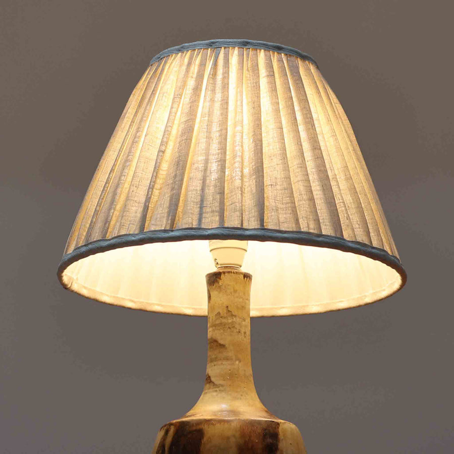 Axella製のこちらのテーブルランプは、素地を生かした陶土の質感に流れるような釉薬のグラデーションが重なり合う有機的な表情が魅力で、ぽってりとした丸みのあるフォルムと細く立ち上がる首部の対比が北欧らしい温かみのある佇まいを生み出すビンテージ品です。手仕事ならではの不均一な釉薬の景色が一点物の存在感を与え、リネンシェードからこぼれる柔らかな灯りがリビングや寝室に落ち着いた雰囲気を添え、経年で深まった陶肌の風合いが空間に自然なアクセントを加えてくれます。