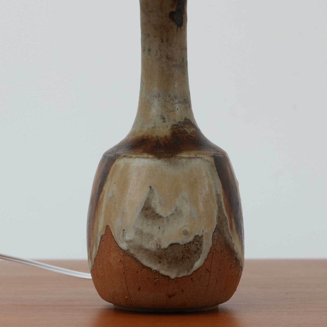 Axella製のこちらのテーブルランプは、素地を生かした陶土の質感に流れるような釉薬のグラデーションが重なり合う有機的な表情が魅力で、ぽってりとした丸みのあるフォルムと細く立ち上がる首部の対比が北欧らしい温かみのある佇まいを生み出すビンテージ品です。手仕事ならではの不均一な釉薬の景色が一点物の存在感を与え、リネンシェードからこぼれる柔らかな灯りがリビングや寝室に落ち着いた雰囲気を添え、経年で深まった陶肌の風合いが空間に自然なアクセントを加えてくれます。