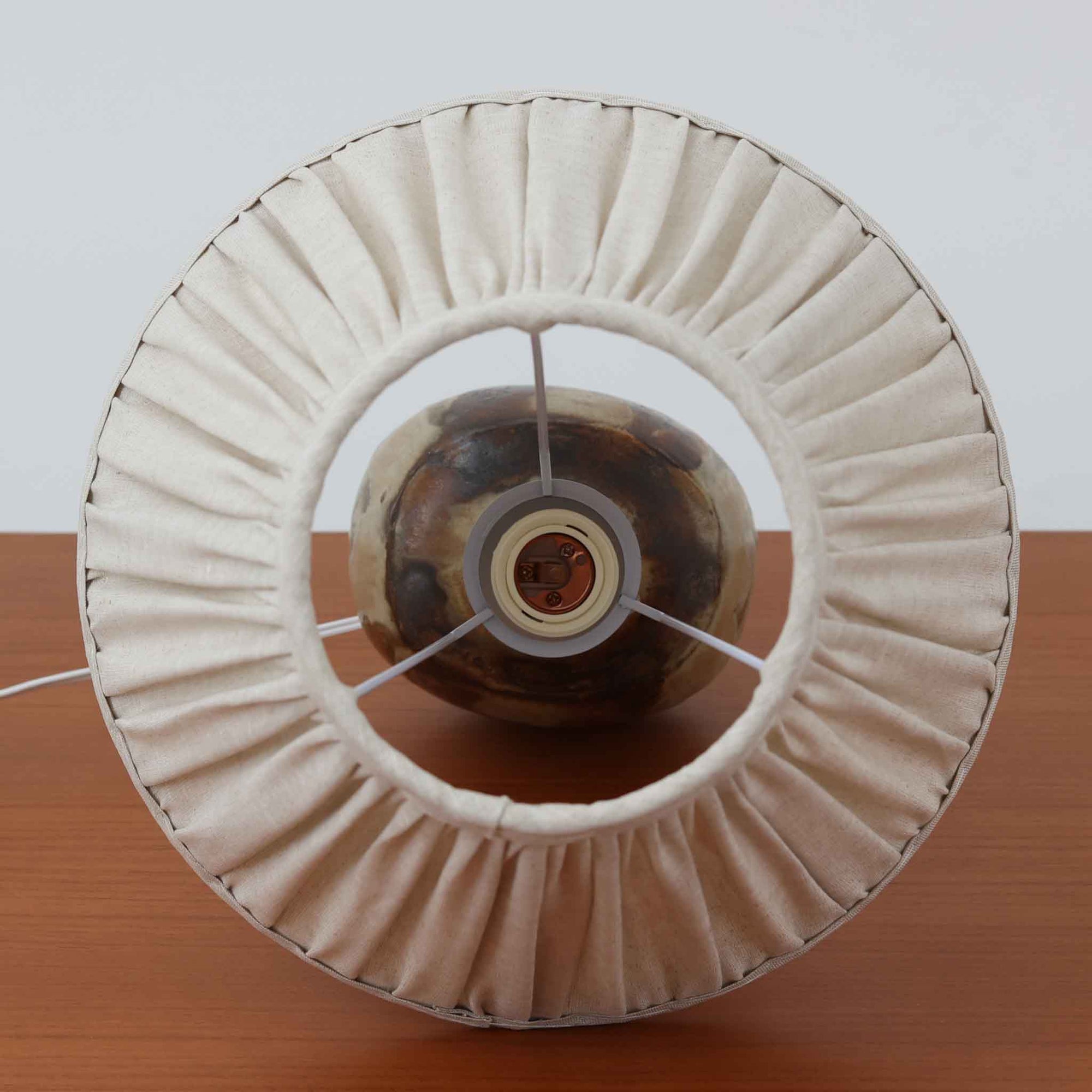 Axella製のこちらのテーブルランプは、素地を生かした陶土の質感に流れるような釉薬のグラデーションが重なり合う有機的な表情が魅力で、ぽってりとした丸みのあるフォルムと細く立ち上がる首部の対比が北欧らしい温かみのある佇まいを生み出すビンテージ品です。手仕事ならではの不均一な釉薬の景色が一点物の存在感を与え、リネンシェードからこぼれる柔らかな灯りがリビングや寝室に落ち着いた雰囲気を添え、経年で深まった陶肌の風合いが空間に自然なアクセントを加えてくれます。