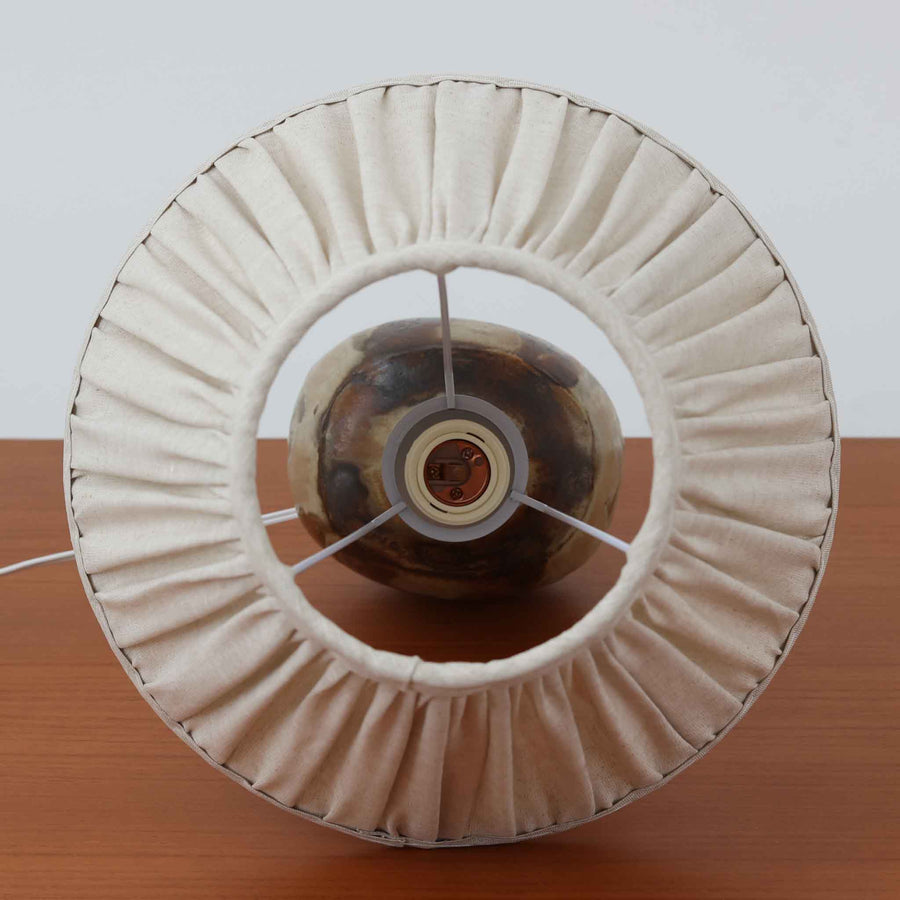 Axella製のこちらのテーブルランプは、素地を生かした陶土の質感に流れるような釉薬のグラデーションが重なり合う有機的な表情が魅力で、ぽってりとした丸みのあるフォルムと細く立ち上がる首部の対比が北欧らしい温かみのある佇まいを生み出すビンテージ品です。手仕事ならではの不均一な釉薬の景色が一点物の存在感を与え、リネンシェードからこぼれる柔らかな灯りがリビングや寝室に落ち着いた雰囲気を添え、経年で深まった陶肌の風合いが空間に自然なアクセントを加えてくれます。