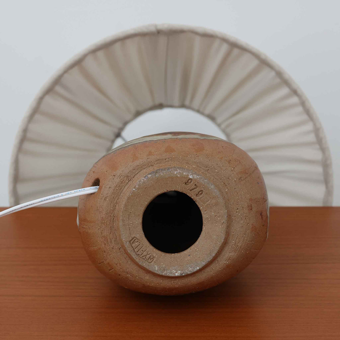 Axella製のこちらのテーブルランプは、素地を生かした陶土の質感に流れるような釉薬のグラデーションが重なり合う有機的な表情が魅力で、ぽってりとした丸みのあるフォルムと細く立ち上がる首部の対比が北欧らしい温かみのある佇まいを生み出すビンテージ品です。手仕事ならではの不均一な釉薬の景色が一点物の存在感を与え、リネンシェードからこぼれる柔らかな灯りがリビングや寝室に落ち着いた雰囲気を添え、経年で深まった陶肌の風合いが空間に自然なアクセントを加えてくれます。