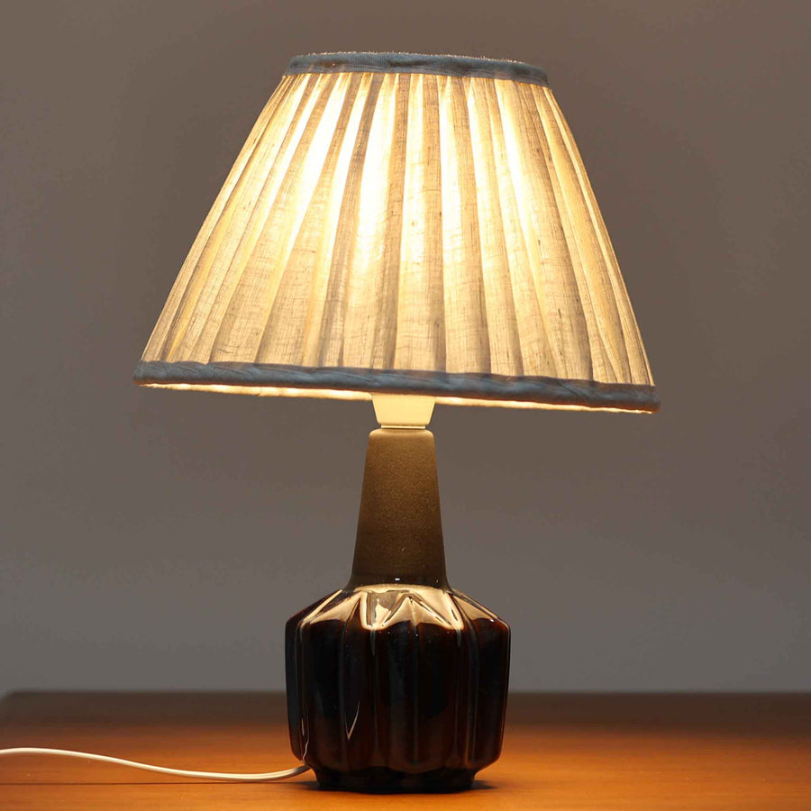 Einar JohansenがSoholm Keramikのために手掛けたモデル「1052」は、濃淡のある深いブルーグラデーションと面取りを施した立体的なフォルムが美しく、上部のマットな質感とのコントラストが上品な存在感を生む北欧ビンテージのテーブルランプです。柔らかく広がるリネンシェードの灯りが陰影豊かな陶肌をやさしく照らし、リビングや寝室のアクセントとして取り入れやすく、経年で深まった釉薬の表情が一点物ならではの味わいを引き立てています。