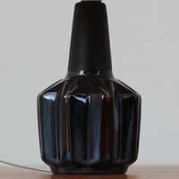 Einar JohansenがSoholm Keramikのために手掛けたモデル「1052」は、濃淡のある深いブルーグラデーションと面取りを施した立体的なフォルムが美しく、上部のマットな質感とのコントラストが上品な存在感を生む北欧ビンテージのテーブルランプです。柔らかく広がるリネンシェードの灯りが陰影豊かな陶肌をやさしく照らし、リビングや寝室のアクセントとして取り入れやすく、経年で深まった釉薬の表情が一点物ならではの味わいを引き立てています。