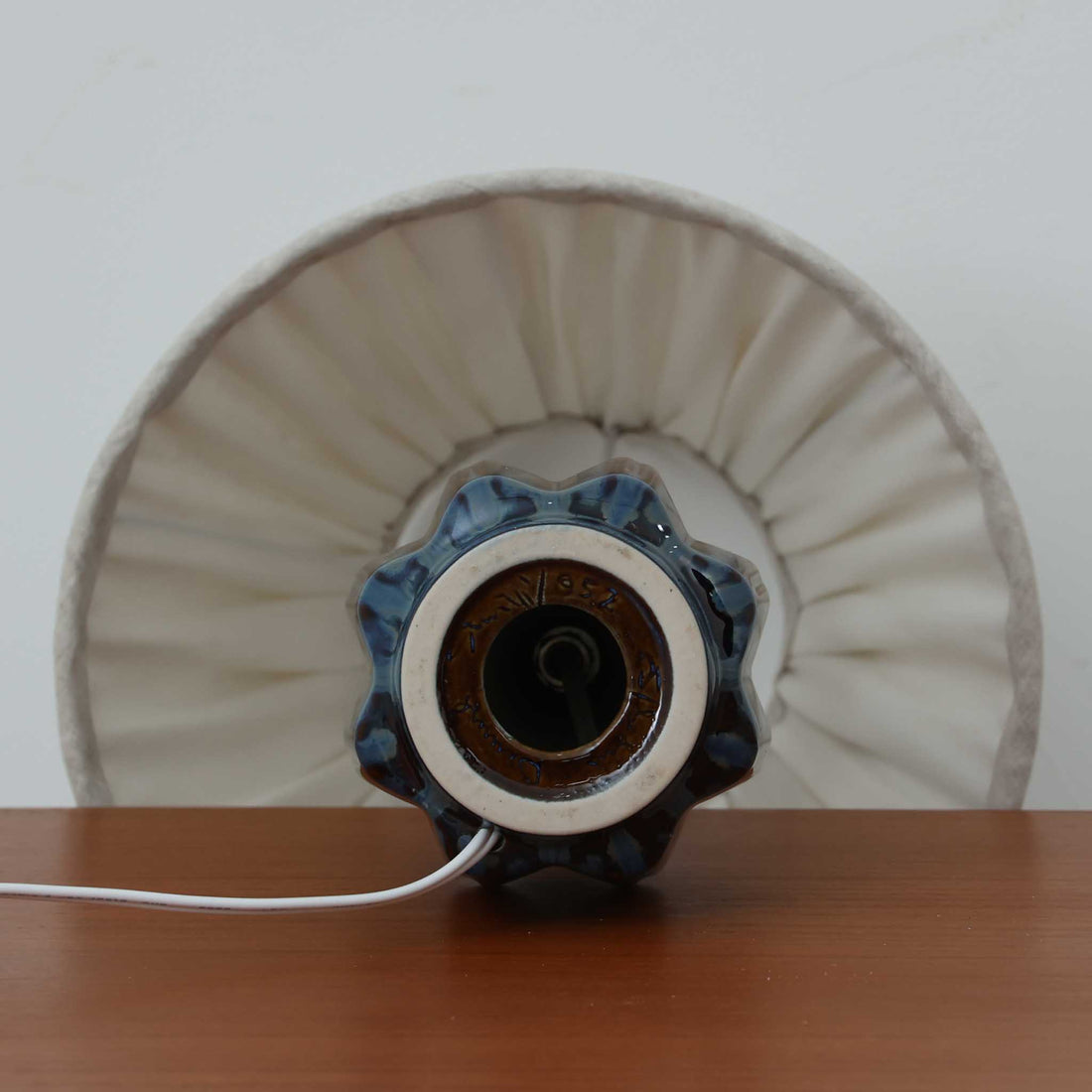 Einar JohansenがSoholm Keramikのために手掛けたモデル「1052」は、濃淡のある深いブルーグラデーションと面取りを施した立体的なフォルムが美しく、上部のマットな質感とのコントラストが上品な存在感を生む北欧ビンテージのテーブルランプです。柔らかく広がるリネンシェードの灯りが陰影豊かな陶肌をやさしく照らし、リビングや寝室のアクセントとして取り入れやすく、経年で深まった釉薬の表情が一点物ならではの味わいを引き立てています。