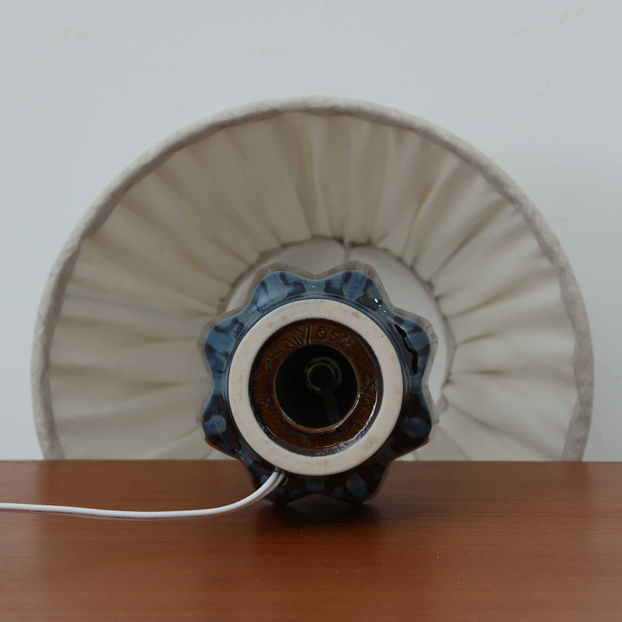 Einar JohansenがSoholm Keramikのために手掛けたモデル「1052」は、濃淡のある深いブルーグラデーションと面取りを施した立体的なフォルムが美しく、上部のマットな質感とのコントラストが上品な存在感を生む北欧ビンテージのテーブルランプです。柔らかく広がるリネンシェードの灯りが陰影豊かな陶肌をやさしく照らし、リビングや寝室のアクセントとして取り入れやすく、経年で深まった釉薬の表情が一点物ならではの味わいを引き立てています。