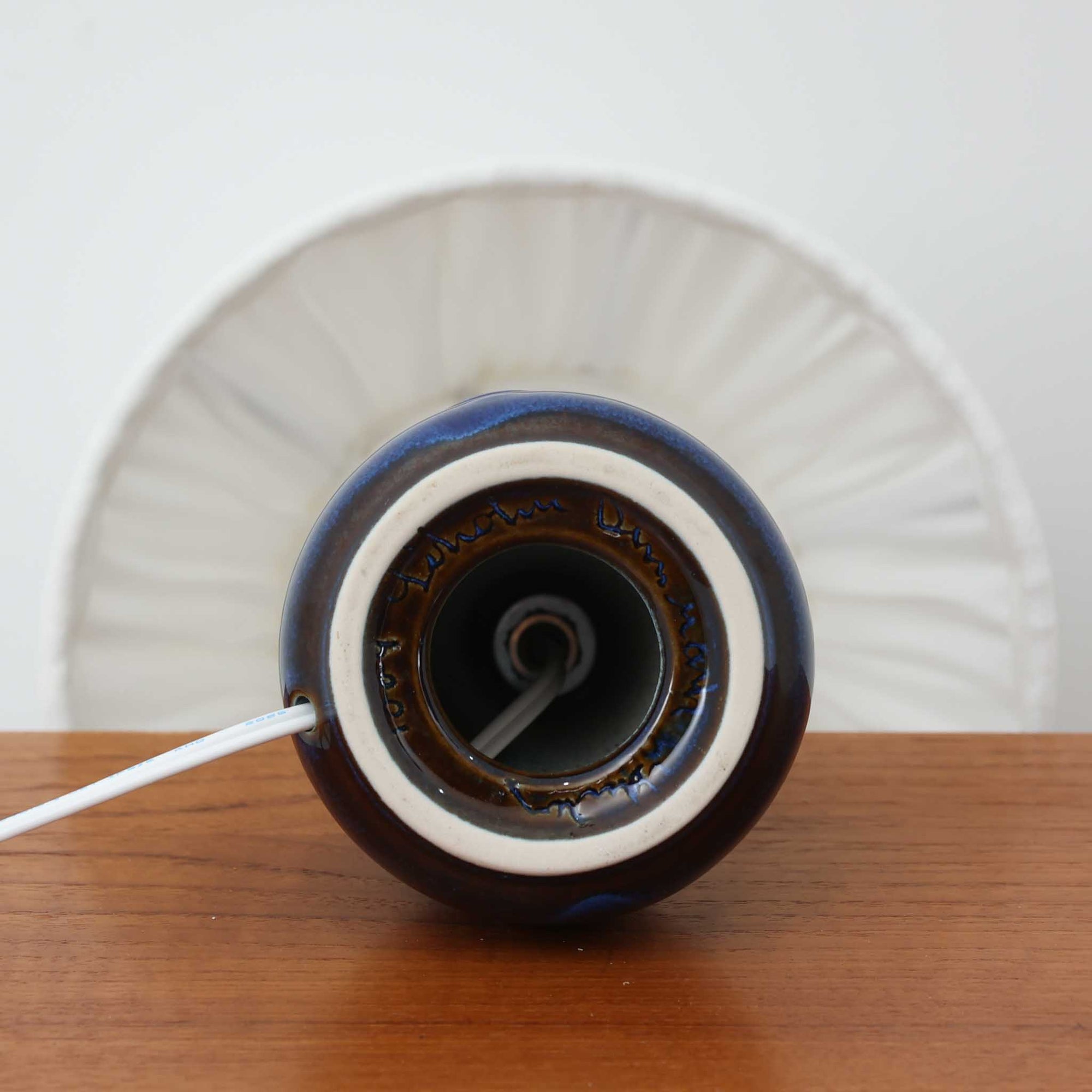 Einar Johansenがデザインし、Soholm Keramikが製作したモデル1004のテーブルランプです。高さ29cmのコンパクトなサイズに、深みあるコバルトブルーの陶磁器ベースと柔らかなリネンシェードを組み合わせた、北欧らしい静謐な美しさが魅力。ベース両側に配された意匠的なレリーフがさりげないアクセントとなり、点灯時にはシェード越しのやわらかな光が艶やかな釉薬の表情をより引き立てます。サイドテーブルやチェスト、ベッドサイドにも取り入れやすく、空間に落ち着いた彩りと温もりを添える一台。Johansenらしい造形美とSoholmの高い陶芸技術が感じられる、希少性の高いビンテージ照明です。
