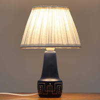 Rigmor Nielsenがデザインし、Soholm Keramikが製作したテーブルランプです。高さ29cmの扱いやすいサイズに、深みのあるネイビーブルーの陶磁器ベースとやわらかなリネンシェードを組み合わせた、北欧らしい静かな存在感が魅力。ベース下部には幾何学的な白いライン文様がぐるりと施され、ミッドセンチュリーらしいリズム感ある意匠が空間のアクセントになります。点灯時にはシェード越しの穏やかな光が陶器のマットな質感と深い青色を引き立て、チェストやベッドサイド、デスク脇にも心地よい温もりを演出。希少なRigmor Nielsen作品ならではの芸術性とビンテージの味わいを楽しめる一台です。