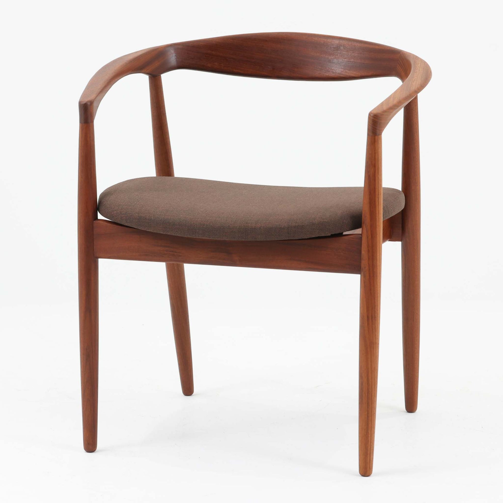 Kai Kristiansenがデザインし、Magnus Olesenが製作したTrojaアームチェアです。アフロモシア材の滑らかな木肌と深みのある色合いが美しく、背からアームへと一体で削り出されたフレームが身体をやさしく包み込みます。わずかに湾曲した笠木や細身の脚部が軽快な印象を与え、立ち座りの動作も自然。張り替え済みの座面は快適な掛け心地を備え、ダイニングや書斎空間に北欧ビンテージならではの気品と造形美をもたらす一脚です。ロゴは、デンマークの家具販売店（小売店）である Brdr. Ellehuus（エルフース兄弟店） のものです。