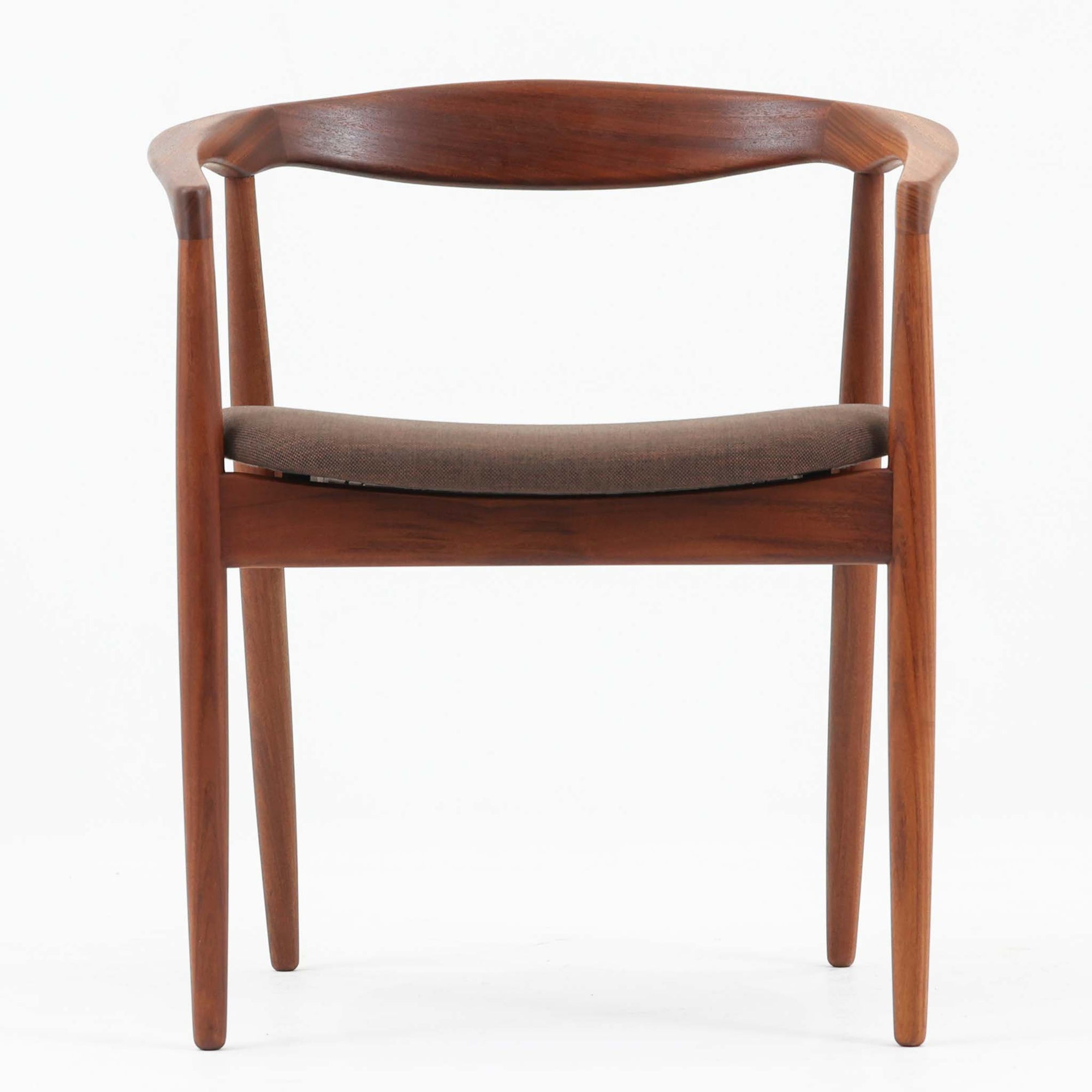 Kai Kristiansenがデザインし、Magnus Olesenが製作したTrojaアームチェアです。アフロモシア材の滑らかな木肌と深みのある色合いが美しく、背からアームへと一体で削り出されたフレームが身体をやさしく包み込みます。わずかに湾曲した笠木や細身の脚部が軽快な印象を与え、立ち座りの動作も自然。張り替え済みの座面は快適な掛け心地を備え、ダイニングや書斎空間に北欧ビンテージならではの気品と造形美をもたらす一脚です。ロゴは、デンマークの家具販売店（小売店）である Brdr. Ellehuus（エルフース兄弟店） のものです。