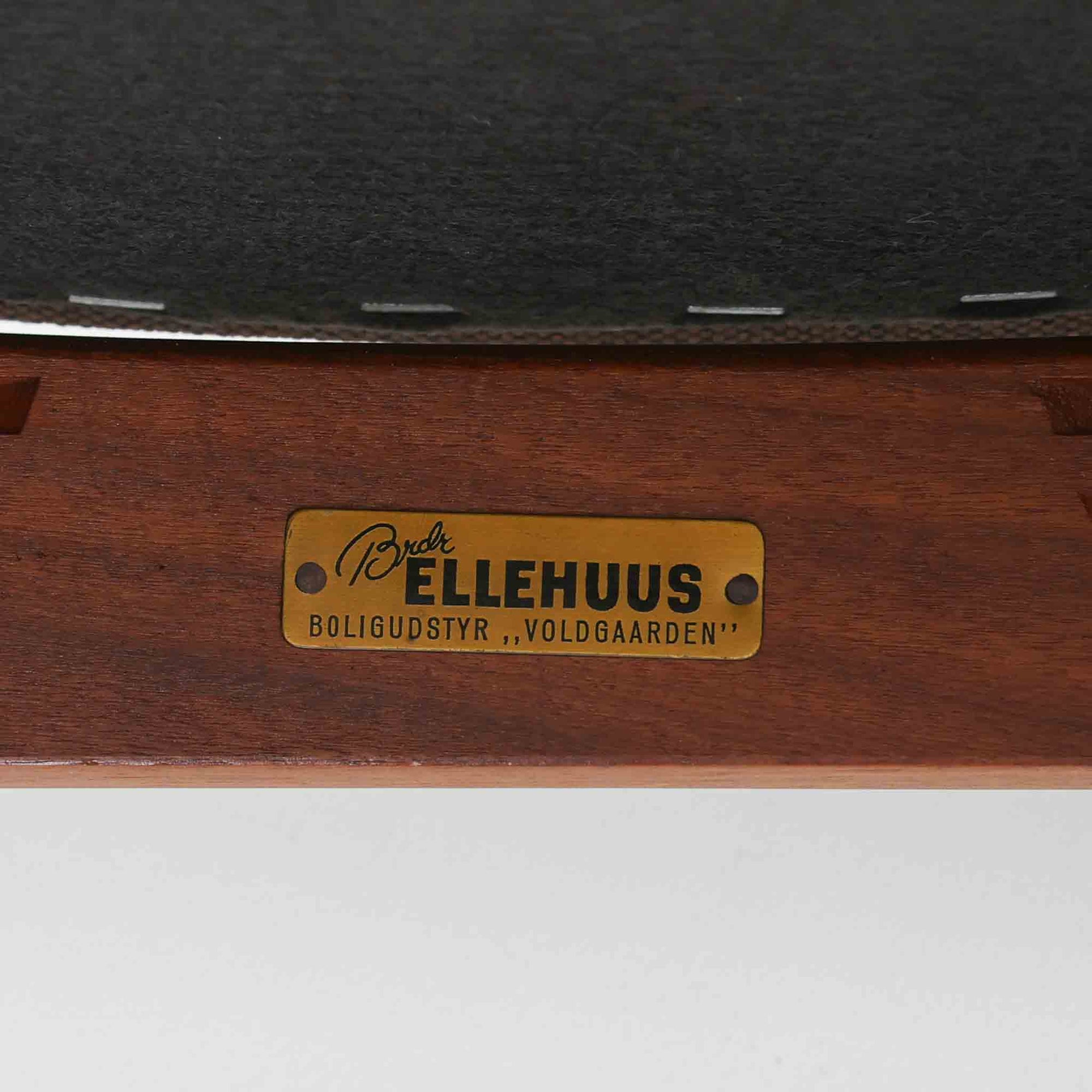 Kai Kristiansenがデザインし、Magnus Olesenが製作したTrojaアームチェアです。アフロモシア材の滑らかな木肌と深みのある色合いが美しく、背からアームへと一体で削り出されたフレームが身体をやさしく包み込みます。わずかに湾曲した笠木や細身の脚部が軽快な印象を与え、立ち座りの動作も自然。張り替え済みの座面は快適な掛け心地を備え、ダイニングや書斎空間に北欧ビンテージならではの気品と造形美をもたらす一脚です。ロゴは、デンマークの家具販売店（小売店）である Brdr. Ellehuus（エルフース兄弟店） のものです。