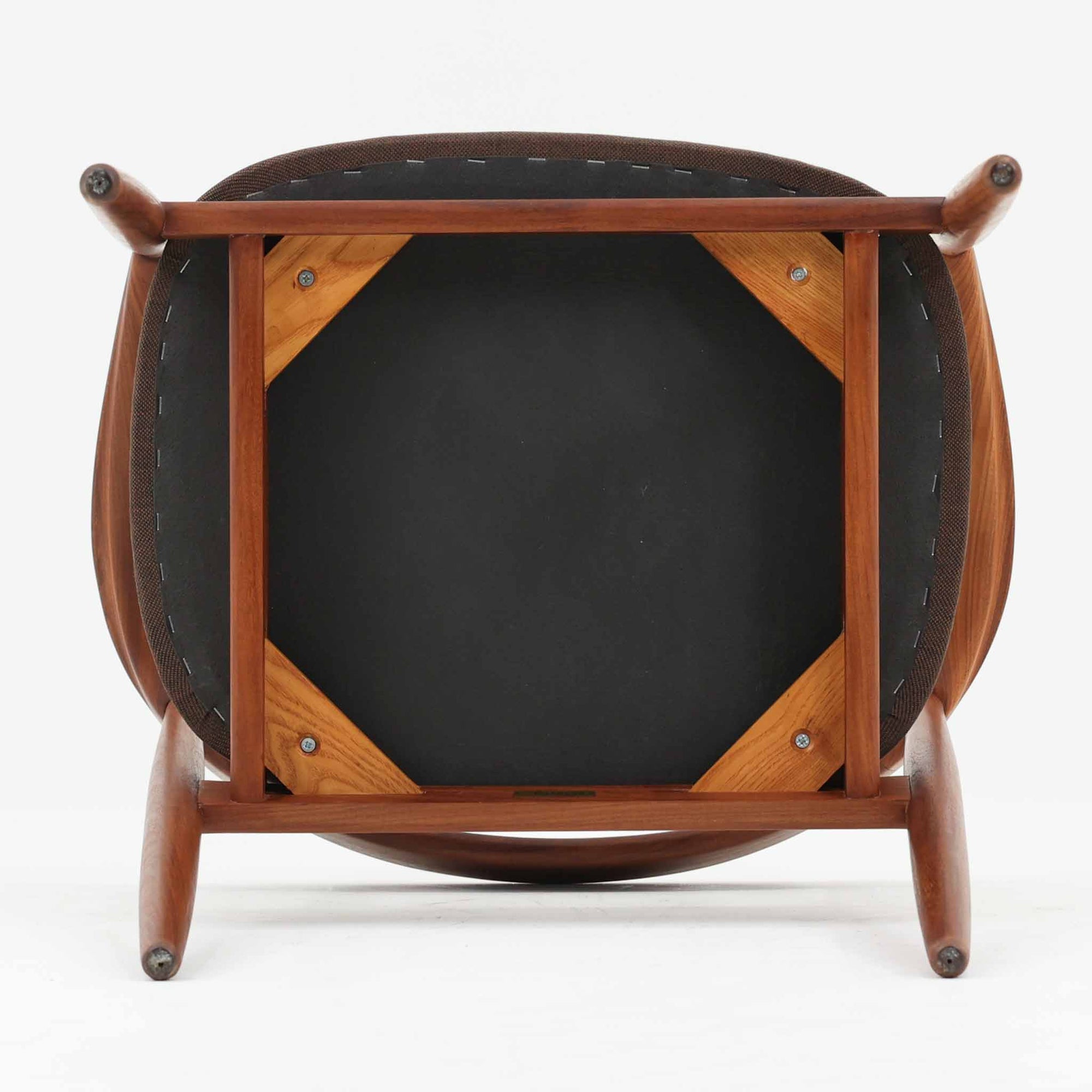 Kai Kristiansenがデザインし、Magnus Olesenが製作したTrojaアームチェアです。アフロモシア材の滑らかな木肌と深みのある色合いが美しく、背からアームへと一体で削り出されたフレームが身体をやさしく包み込みます。わずかに湾曲した笠木や細身の脚部が軽快な印象を与え、立ち座りの動作も自然。張り替え済みの座面は快適な掛け心地を備え、ダイニングや書斎空間に北欧ビンテージならではの気品と造形美をもたらす一脚です。ロゴは、デンマークの家具販売店（小売店）である Brdr. Ellehuus（エルフース兄弟店） のものです。