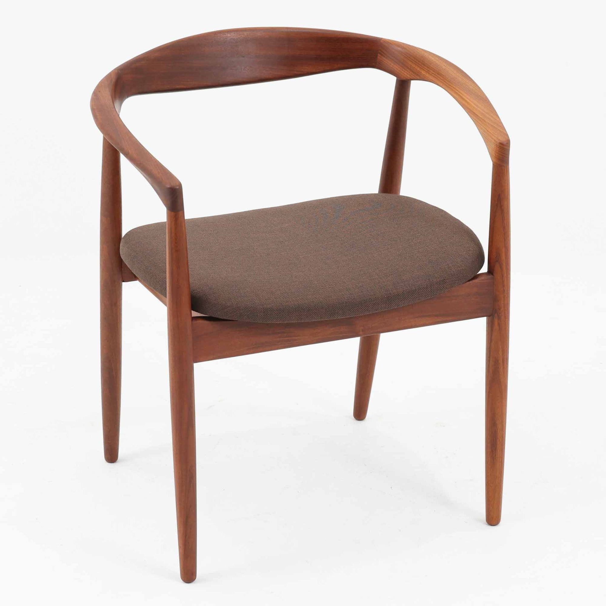 Kai Kristiansenがデザインし、Magnus Olesenが製作したTrojaアームチェアです。アフロモシア材の滑らかな木肌と深みのある色合いが美しく、背からアームへと一体で削り出されたフレームが身体をやさしく包み込みます。わずかに湾曲した笠木や細身の脚部が軽快な印象を与え、立ち座りの動作も自然。張り替え済みの座面は快適な掛け心地を備え、ダイニングや書斎空間に北欧ビンテージならではの気品と造形美をもたらす一脚です。ロゴは、デンマークの家具販売店（小売店）である Brdr. Ellehuus（エルフース兄弟店） のものです。