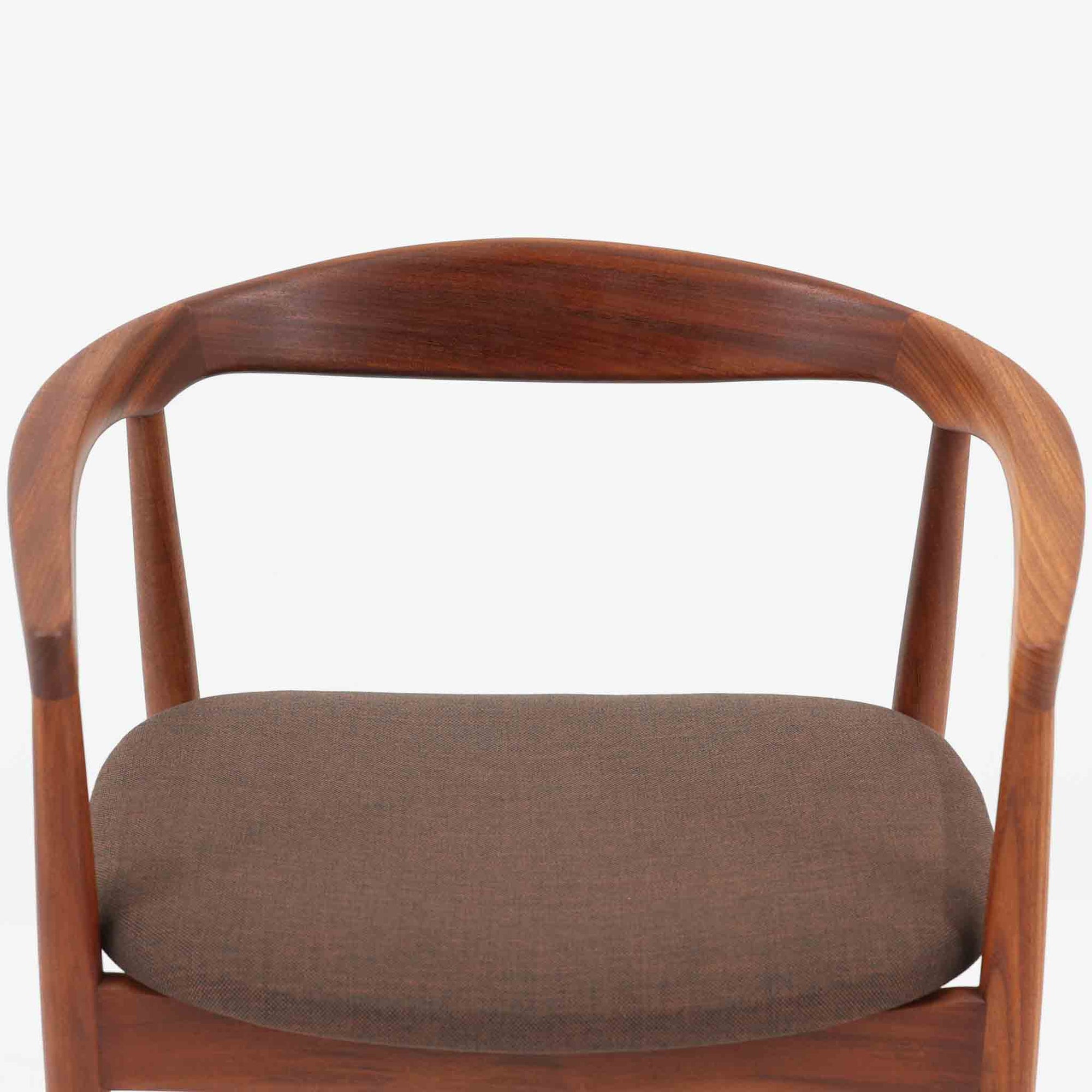 Kai Kristiansenがデザインし、Magnus Olesenが製作したTrojaアームチェアです。アフロモシア材の滑らかな木肌と深みのある色合いが美しく、背からアームへと一体で削り出されたフレームが身体をやさしく包み込みます。わずかに湾曲した笠木や細身の脚部が軽快な印象を与え、立ち座りの動作も自然。張り替え済みの座面は快適な掛け心地を備え、ダイニングや書斎空間に北欧ビンテージならではの気品と造形美をもたらす一脚です。ロゴは、デンマークの家具販売店（小売店）である Brdr. Ellehuus（エルフース兄弟店） のものです。