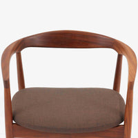 Kai Kristiansenがデザインし、Magnus Olesenが製作したTrojaアームチェアです。アフロモシア材の滑らかな木肌と深みのある色合いが美しく、背からアームへと一体で削り出されたフレームが身体をやさしく包み込みます。わずかに湾曲した笠木や細身の脚部が軽快な印象を与え、立ち座りの動作も自然。張り替え済みの座面は快適な掛け心地を備え、ダイニングや書斎空間に北欧ビンテージならではの気品と造形美をもたらす一脚です。ロゴは、デンマークの家具販売店（小売店）である Brdr. Ellehuus（エルフース兄弟店） のものです。