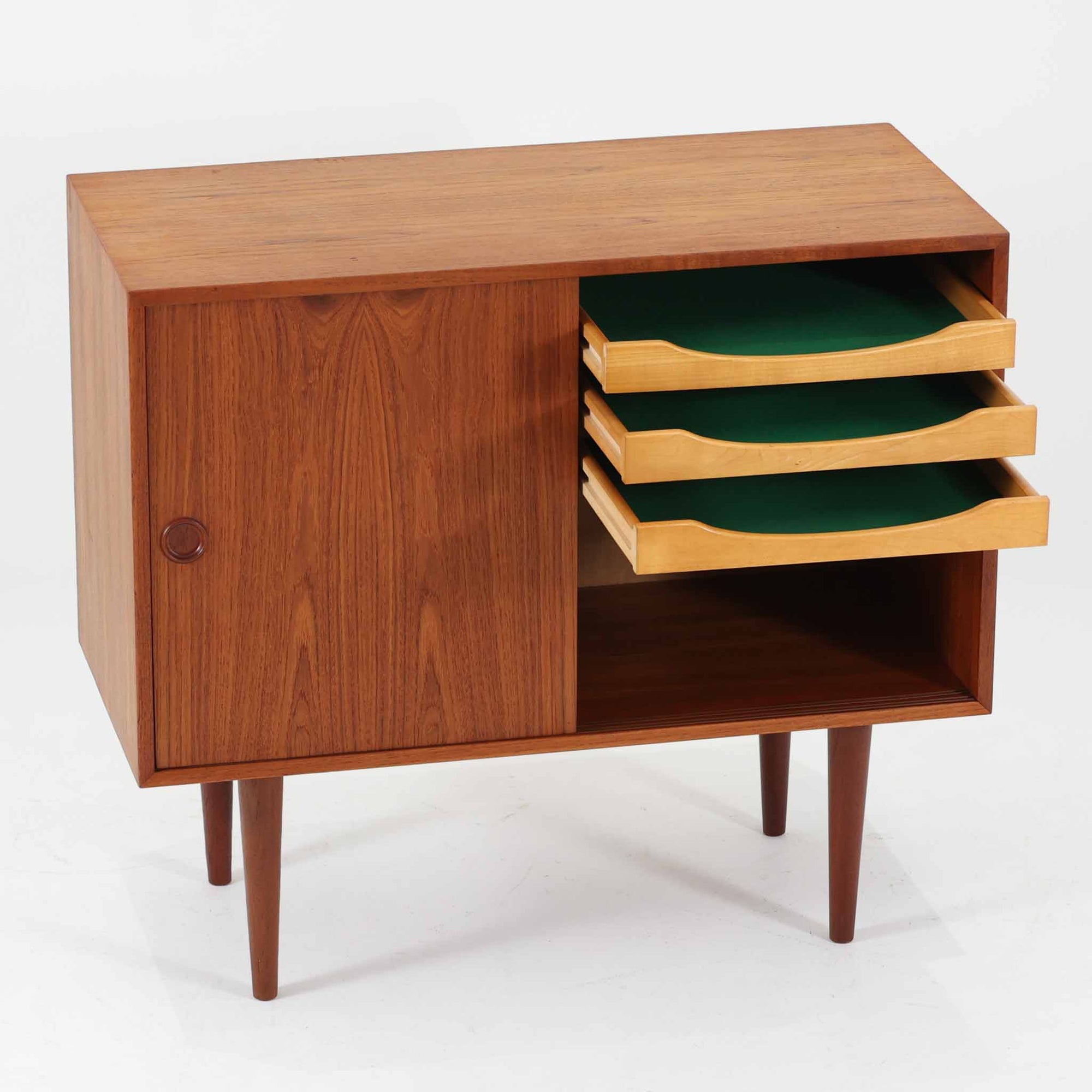 Kai Kristiansenがデザインし、Feldballes Mobelfabrikが製作した幅86cmの小ぶりなボードです。チーク材の美しい木目を活かした端正な箱型フォルムに、丸い引き手付きの引き戸がアクセントを添えます。内部には棚とトレー収納を備え、書類や小物を整理しやすい実用的な構造。すらりと伸びる脚部が軽やかさを演出し、限られた空間にも取り入れやすいサイズ感です。経年により深みを増した木肌が、北欧ビンテージならではの温もりと存在感を感じさせます。