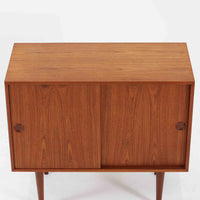 Kai Kristiansenがデザインし、Feldballes Mobelfabrikが製作した幅86cmの小ぶりなボードです。チーク材の美しい木目を活かした端正な箱型フォルムに、丸い引き手付きの引き戸がアクセントを添えます。内部には棚とトレー収納を備え、書類や小物を整理しやすい実用的な構造。すらりと伸びる脚部が軽やかさを演出し、限られた空間にも取り入れやすいサイズ感です。経年により深みを増した木肌が、北欧ビンテージならではの温もりと存在感を感じさせます。