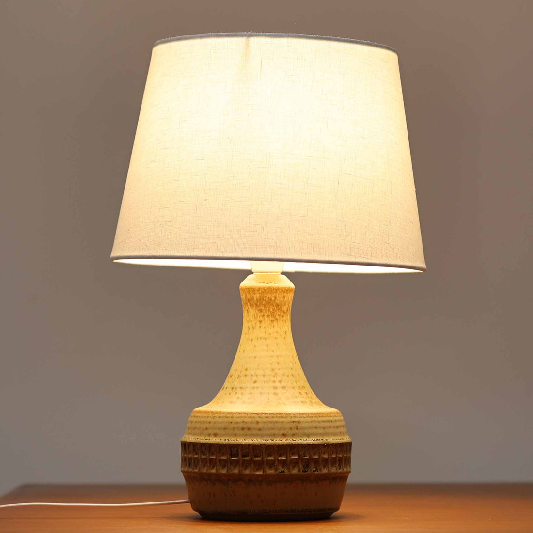 Soholm Keramik（スーホルム・セラミック）製のテーブルランプです。落ち着いたブラウンの陶磁器ボディに幾何学模様の装飾が施され、シンプルながらも存在感のあるデザインが魅力です。高さ38cmと扱いやすいサイズ感で、リビングや寝室のサイドテーブルに心地よい灯りを添えてくれます。北欧ビンテージならではの温かみある質感が、空間に柔らかな雰囲気をもたらします。