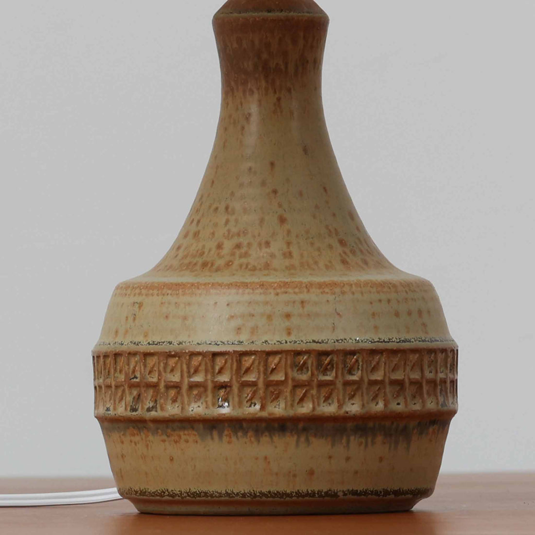 Soholm Keramik（スーホルム・セラミック）製のテーブルランプです。落ち着いたブラウンの陶磁器ボディに幾何学模様の装飾が施され、シンプルながらも存在感のあるデザインが魅力です。高さ38cmと扱いやすいサイズ感で、リビングや寝室のサイドテーブルに心地よい灯りを添えてくれます。北欧ビンテージならではの温かみある質感が、空間に柔らかな雰囲気をもたらします。