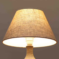 Chris HaslevがJetiのために手掛けたこちらのテーブルランプは、太陽を思わせるレリーフ模様をまとった陶器ベースと、素朴な土肌と釉薬の濃淡が織りなす豊かな表情が魅力で、コンパクトながら存在感を放つ北欧ビンテージ品です。上部のマットな質感が造形を引き締め、リネンシェード越しに広がるあたたかな灯りが空間をやさしく包み込み、リビングやベッドサイドのアクセントとして取り入れやすい一台に仕上がっています。