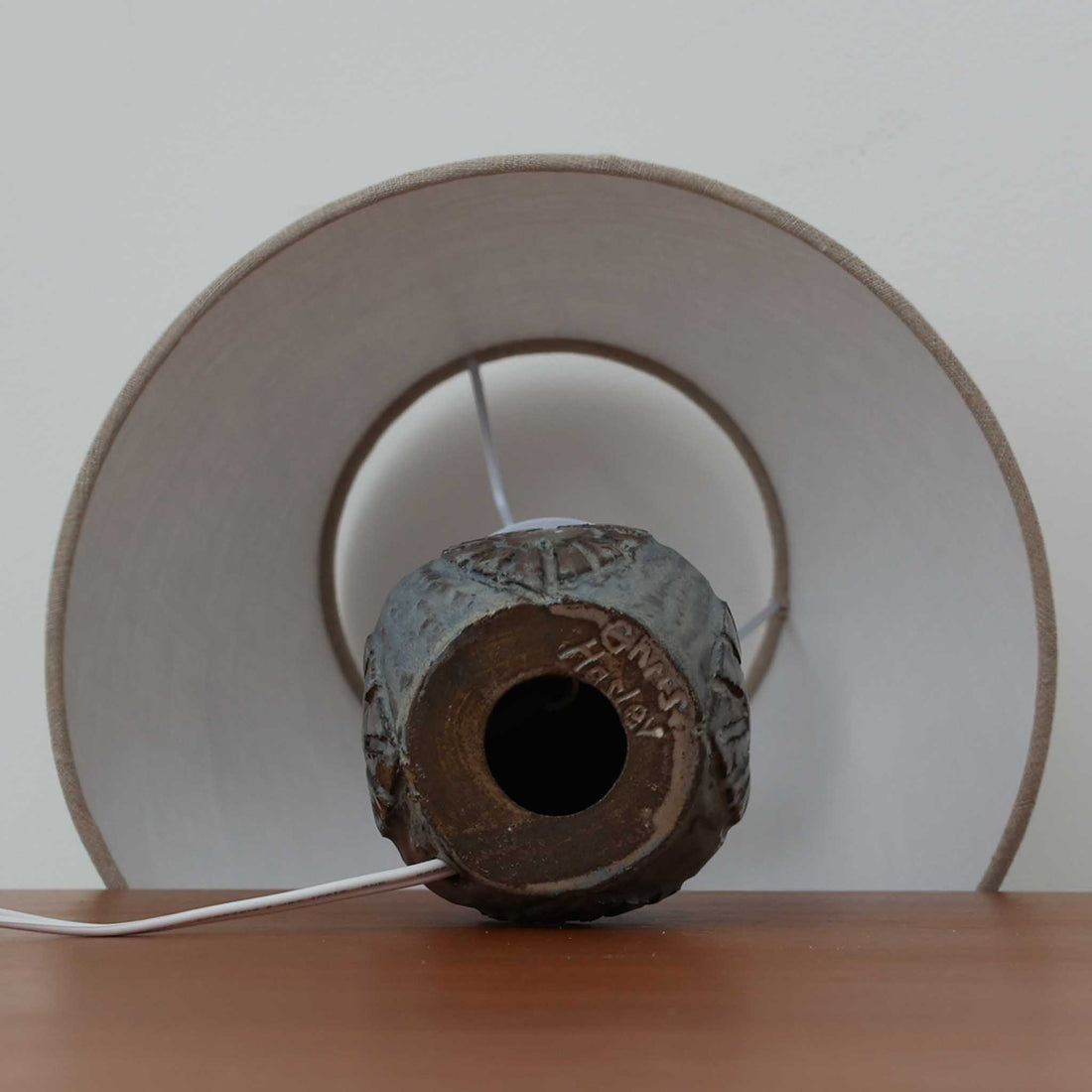 Chris HaslevがJetiのために手掛けたこちらのテーブルランプは、太陽を思わせるレリーフ模様をまとった陶器ベースと、素朴な土肌と釉薬の濃淡が織りなす豊かな表情が魅力で、コンパクトながら存在感を放つ北欧ビンテージ品です。上部のマットな質感が造形を引き締め、リネンシェード越しに広がるあたたかな灯りが空間をやさしく包み込み、リビングやベッドサイドのアクセントとして取り入れやすい一台に仕上がっています。