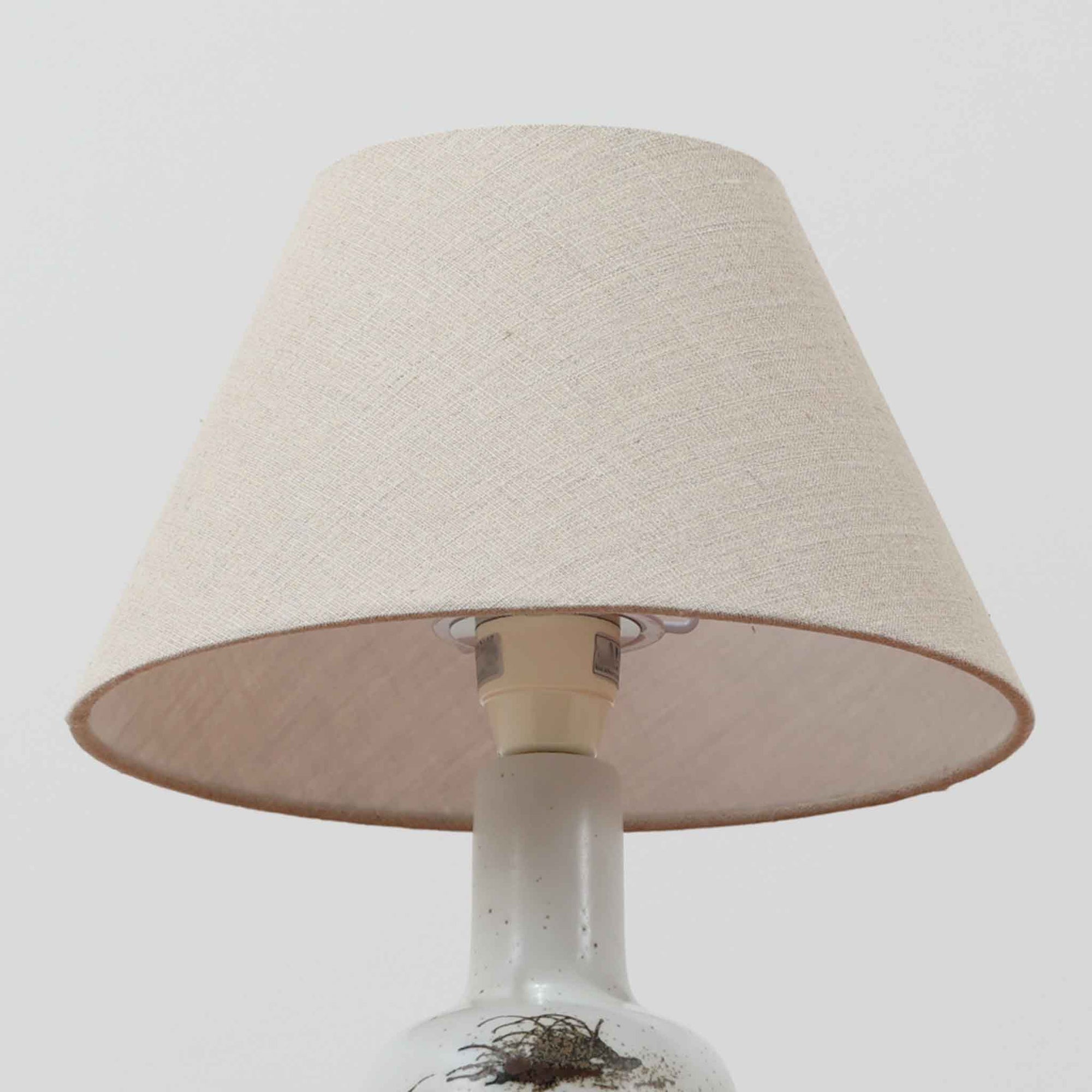 Nils Thorsson（ニルス・トールソン）によるRoyal Copenhagen（ロイヤルコペンハーゲン）の「DIANA」シリーズのテーブルランプは、白磁に繊細な草花や鳥の情景が描かれた静謐な佇まいが魅力で、淡い釉調が経年によりさらに深みを増したビンテージならではの味わいを感じさせます。柔らかく丸みを帯びたベースから伸びるすっきりとした首部のプロポーションが美しく、リネンシェードを通した穏やかな灯りが空間に上質な落ち着きを添えます。高さ32cmとコンパクトで取り入れやすく、ベッドサイドや読書灯としても活躍する、北欧陶芸の上品さが詰まった一台です。