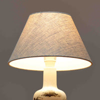 Nils Thorsson（ニルス・トールソン）によるRoyal Copenhagen（ロイヤルコペンハーゲン）の「DIANA」シリーズのテーブルランプは、白磁に繊細な草花や鳥の情景が描かれた静謐な佇まいが魅力で、淡い釉調が経年によりさらに深みを増したビンテージならではの味わいを感じさせます。柔らかく丸みを帯びたベースから伸びるすっきりとした首部のプロポーションが美しく、リネンシェードを通した穏やかな灯りが空間に上質な落ち着きを添えます。高さ32cmとコンパクトで取り入れやすく、ベッドサイドや読書灯としても活躍する、北欧陶芸の上品さが詰まった一台です。