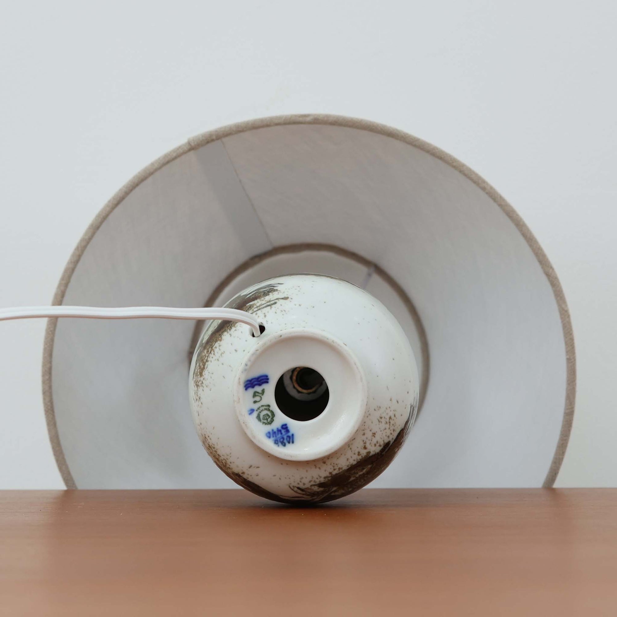 Nils Thorsson（ニルス・トールソン）によるRoyal Copenhagen（ロイヤルコペンハーゲン）の「DIANA」シリーズのテーブルランプは、白磁に繊細な草花や鳥の情景が描かれた静謐な佇まいが魅力で、淡い釉調が経年によりさらに深みを増したビンテージならではの味わいを感じさせます。柔らかく丸みを帯びたベースから伸びるすっきりとした首部のプロポーションが美しく、リネンシェードを通した穏やかな灯りが空間に上質な落ち着きを添えます。高さ32cmとコンパクトで取り入れやすく、ベッドサイドや読書灯としても活躍する、北欧陶芸の上品さが詰まった一台です。